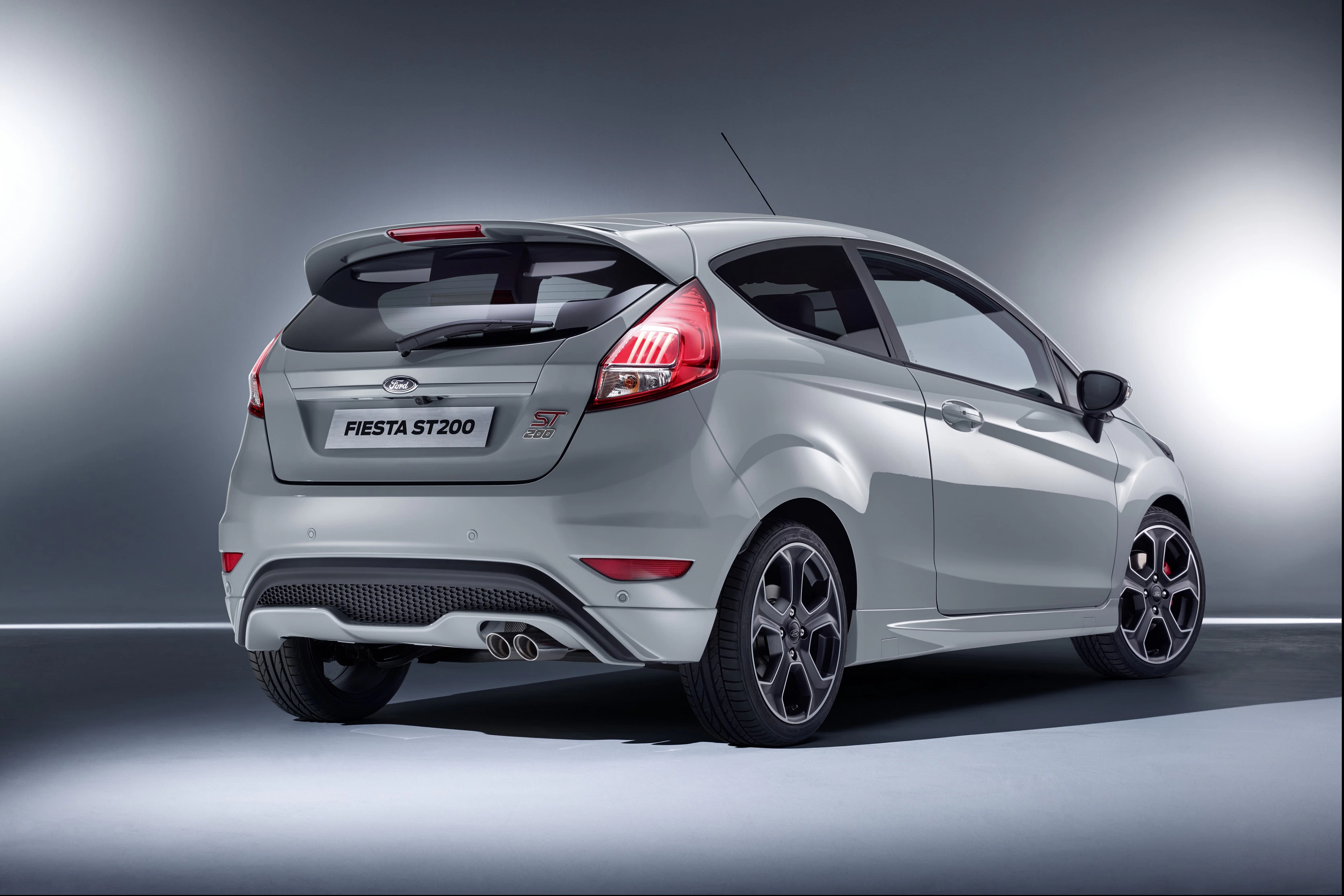 Silberner Ford Fiesta ST200 von hinten, zeigt sportliches Design, Doppelauspuff und markante Rückleuchten vor grauem Hintergrund.