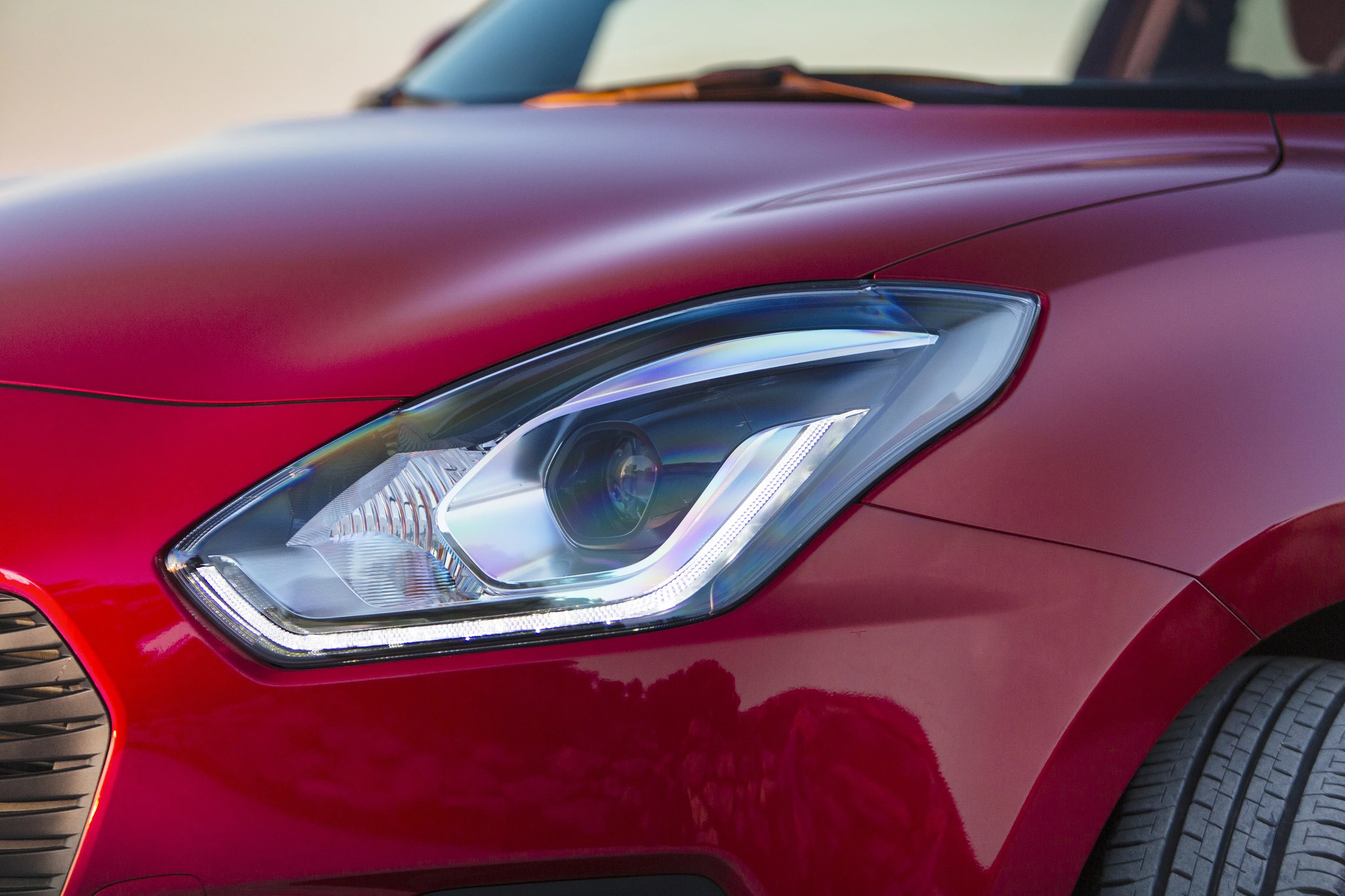 Nahaufnahme eines roten Autos mit modernem Scheinwerferdesign, das die Lichtreflexionen in der glatten Karosserie zeigt.