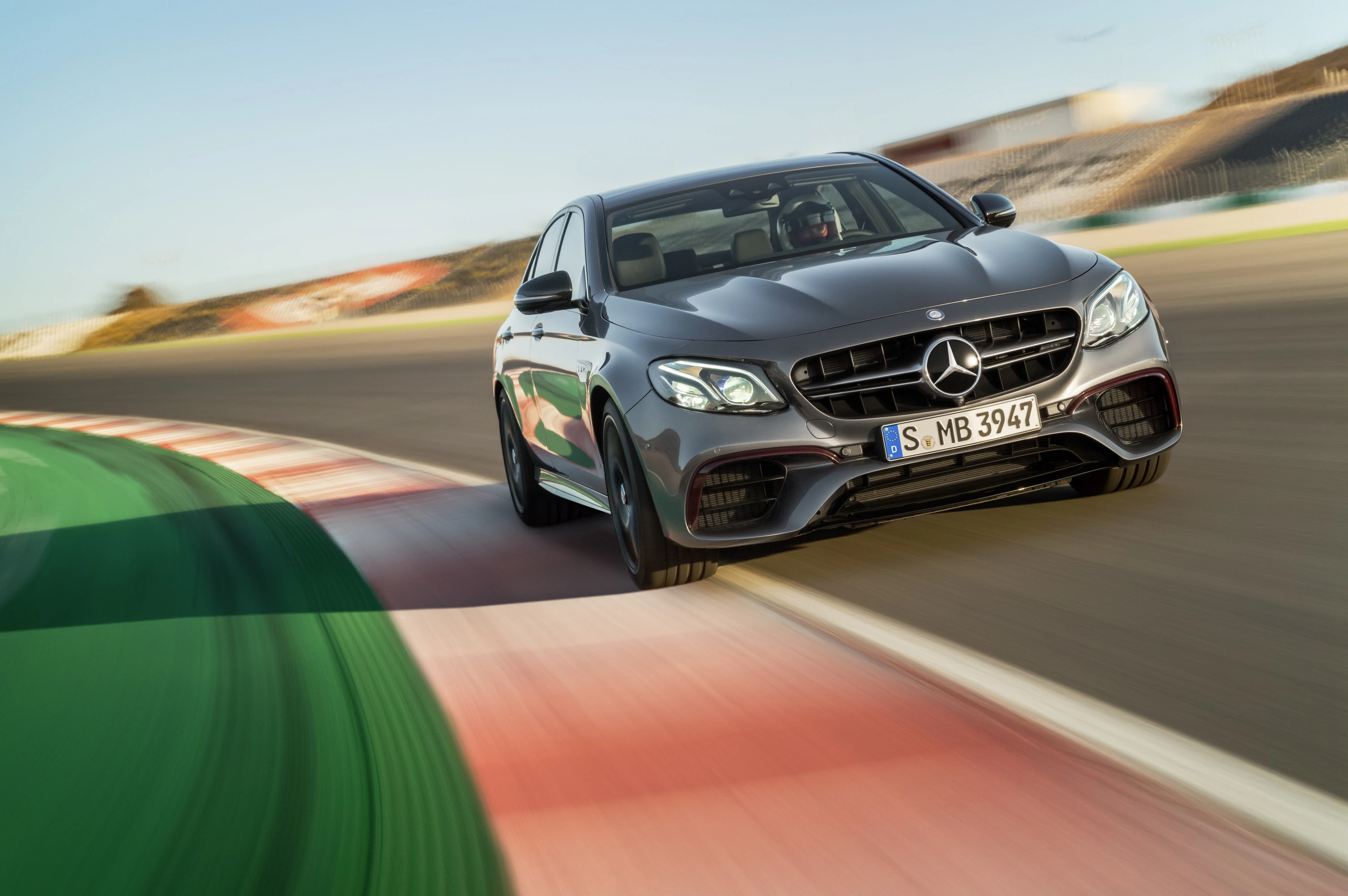 Dunkelgraues Auto fährt dynamisch auf einer Rennstrecke durch eine Kurve, mit unscharfem Hintergrund für Geschwindigkeitseffekt.