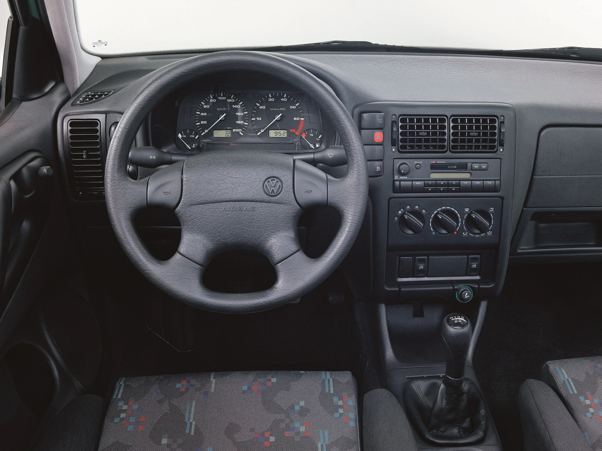 Innenraum eines Autos mit Lenkrad, Tachometer und Bedienelementen. Ein manuelles Getriebe und ein klassisches Armaturenbrett sind sichtbar.