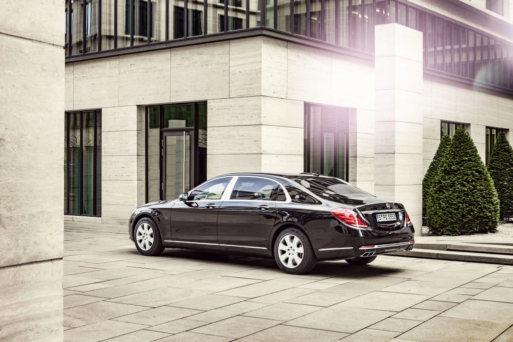 Schwarze Luxuslimousine vor modernem Gebäude mit großen Fenstern und geometrischer Architektur. Helle Steinmauern und gepflegte Büsche.
