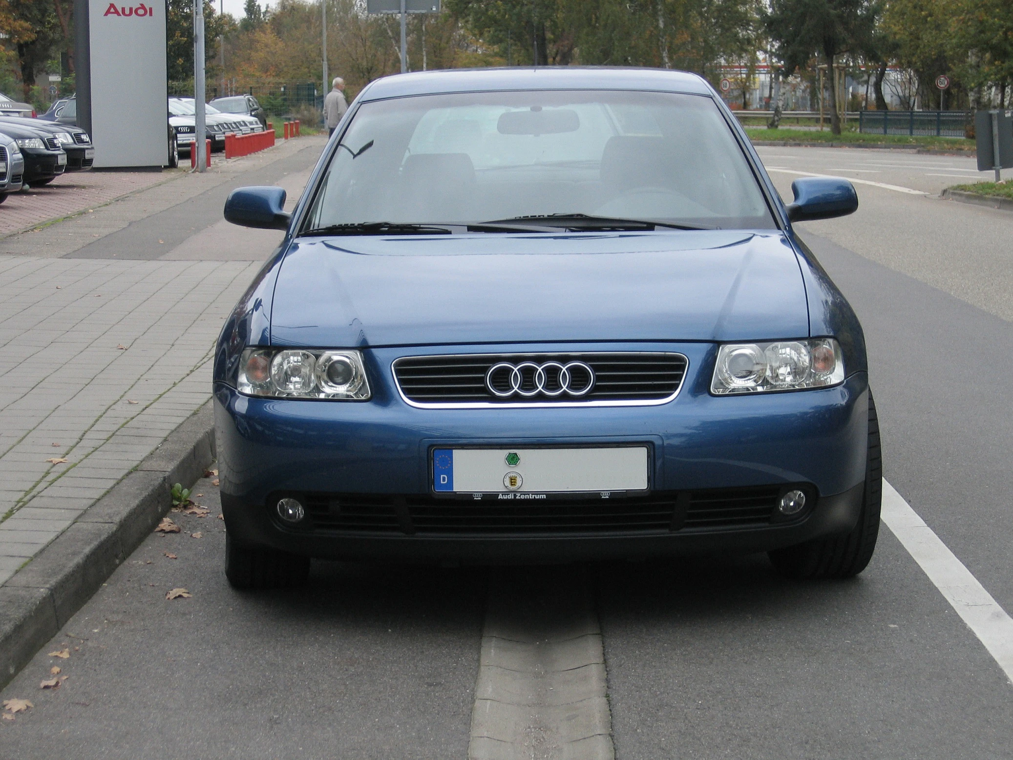 Blauer Audi parkt halb auf dem Bürgersteig und halb auf der Straße. Vorderansicht bei bewölktem Wetter.
