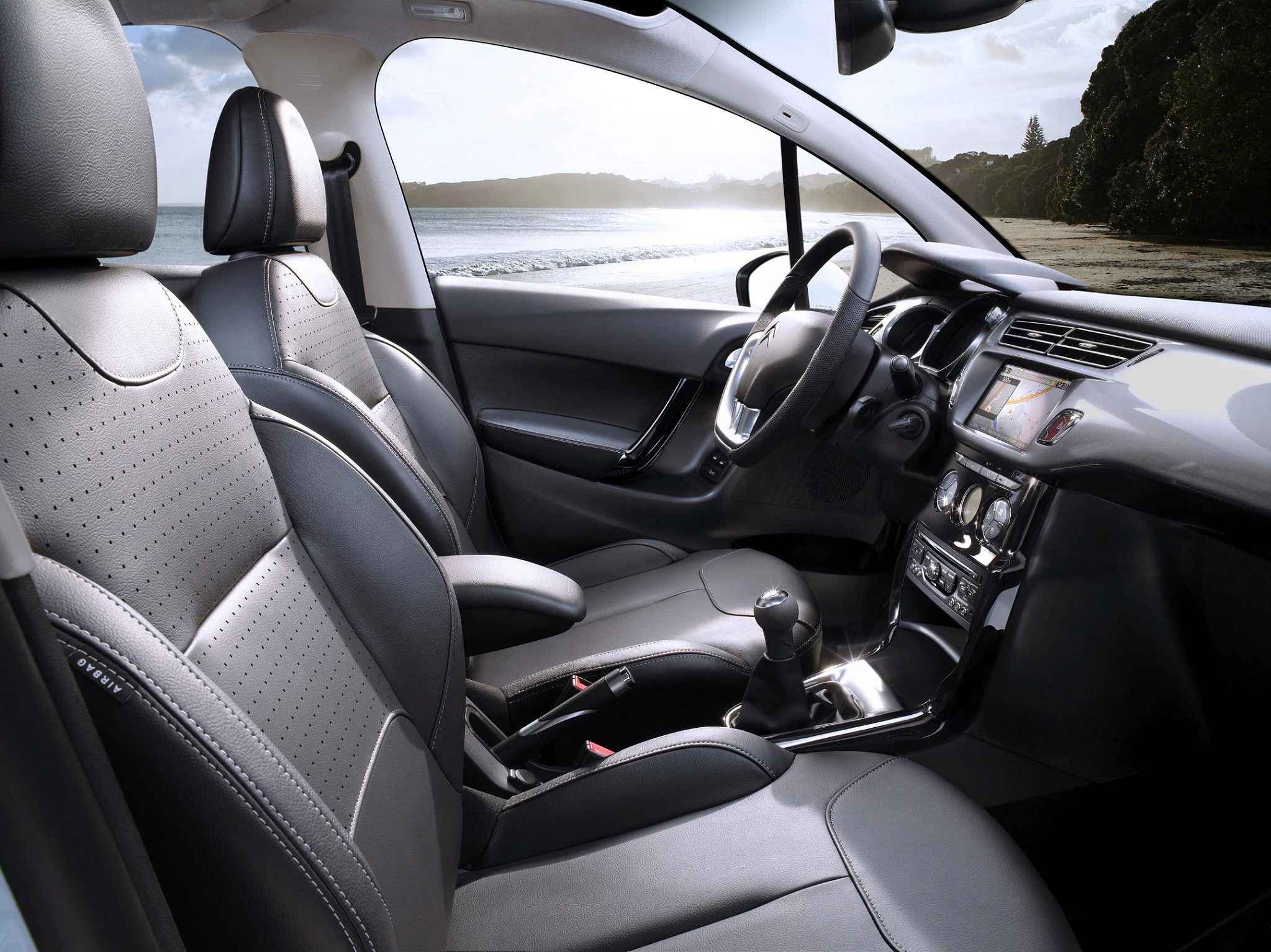 Innenraum eines modernen Autos mit Ledersitzen und Armaturenbrett. Blick aus den Fenstern zeigt Strand und Meer.