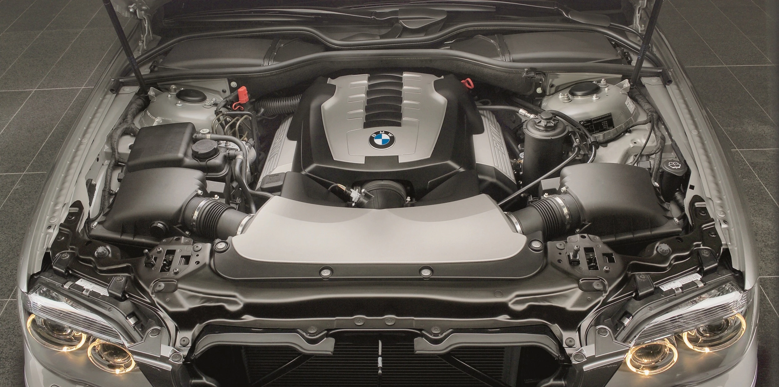 Auto mit geöffneter Motorhaube zeigt BMW-Motor. Detallierte Ansicht der technischen Komponenten und des Markenlogos.