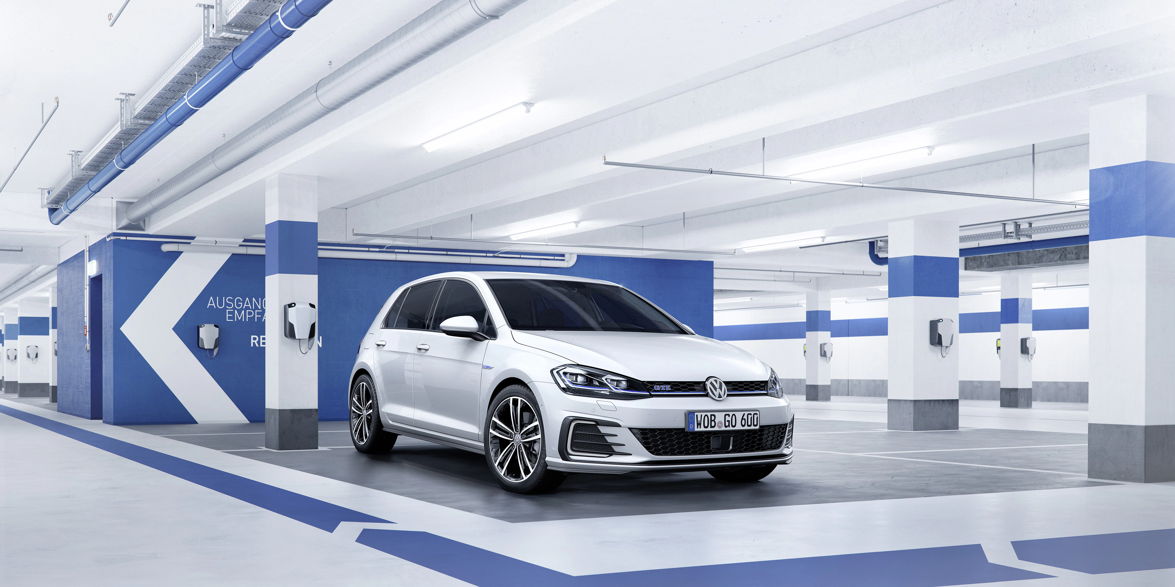 Weißer VW Golf steht in einer modernen, leeren Tiefgarage mit blauen Streifen und Ladestationen an den Wänden.