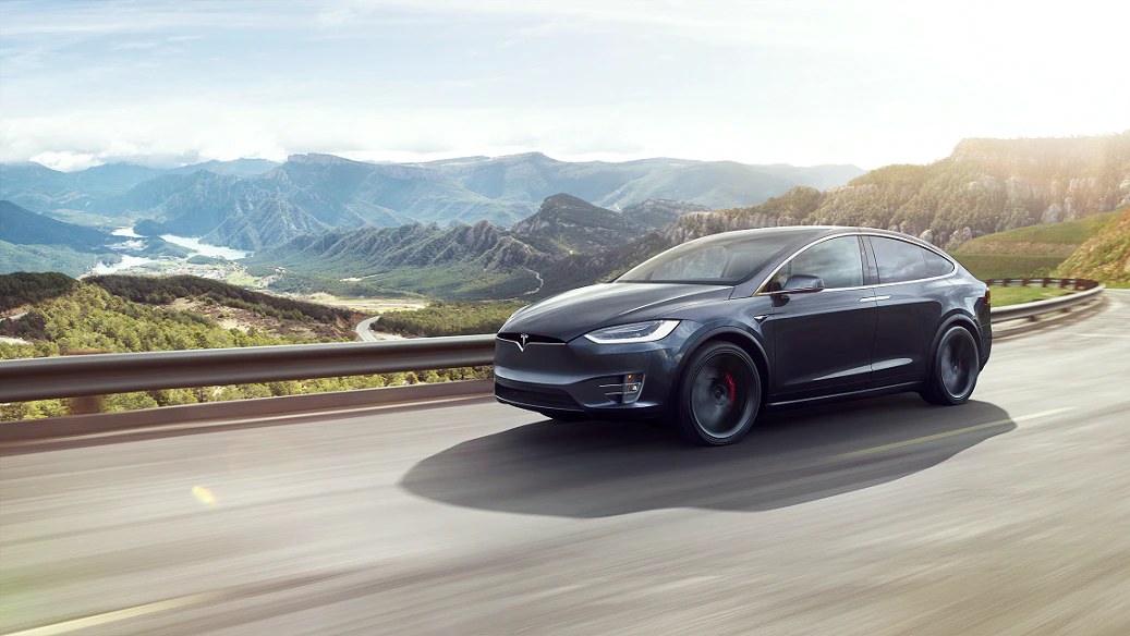Ein schwarzer Tesla fährt auf einer kurvigen Bergstraße bei sonnigem Wetter, umgeben von Berglandschaften.