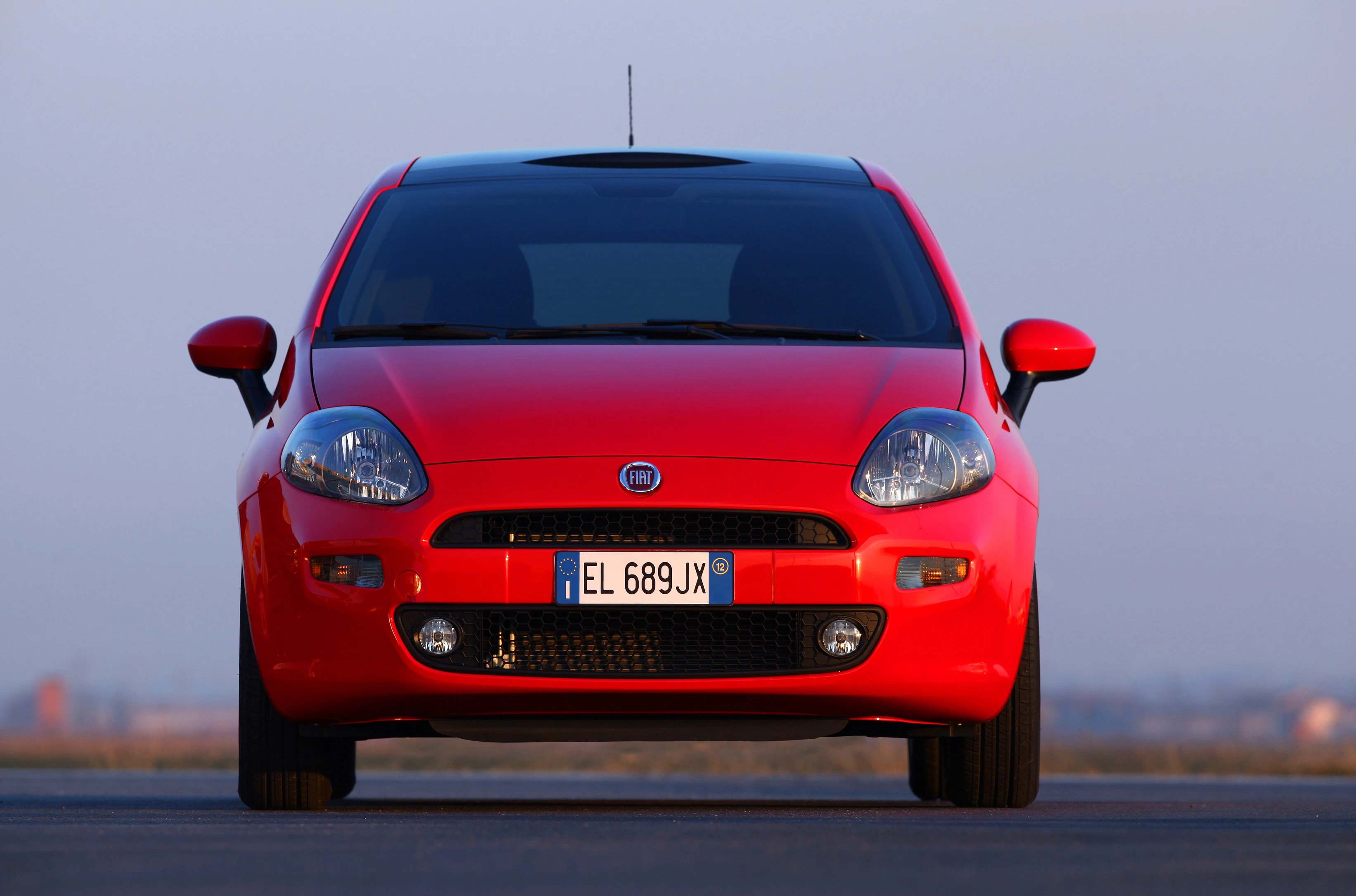 Roter Fiat Punto fotografiert frontal auf einer Straße, mit italienischem Kennzeichen und blauem Himmel im Hintergrund.