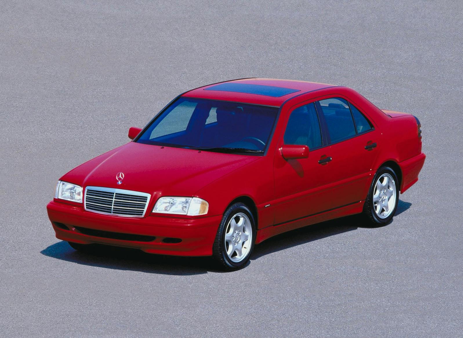 Roter Mercedes-Benz C-Klasse Limousine, geparkt auf grauem Asphalt, Vorderansicht. Automobil mit Sonnendach und silbernen Felgen.