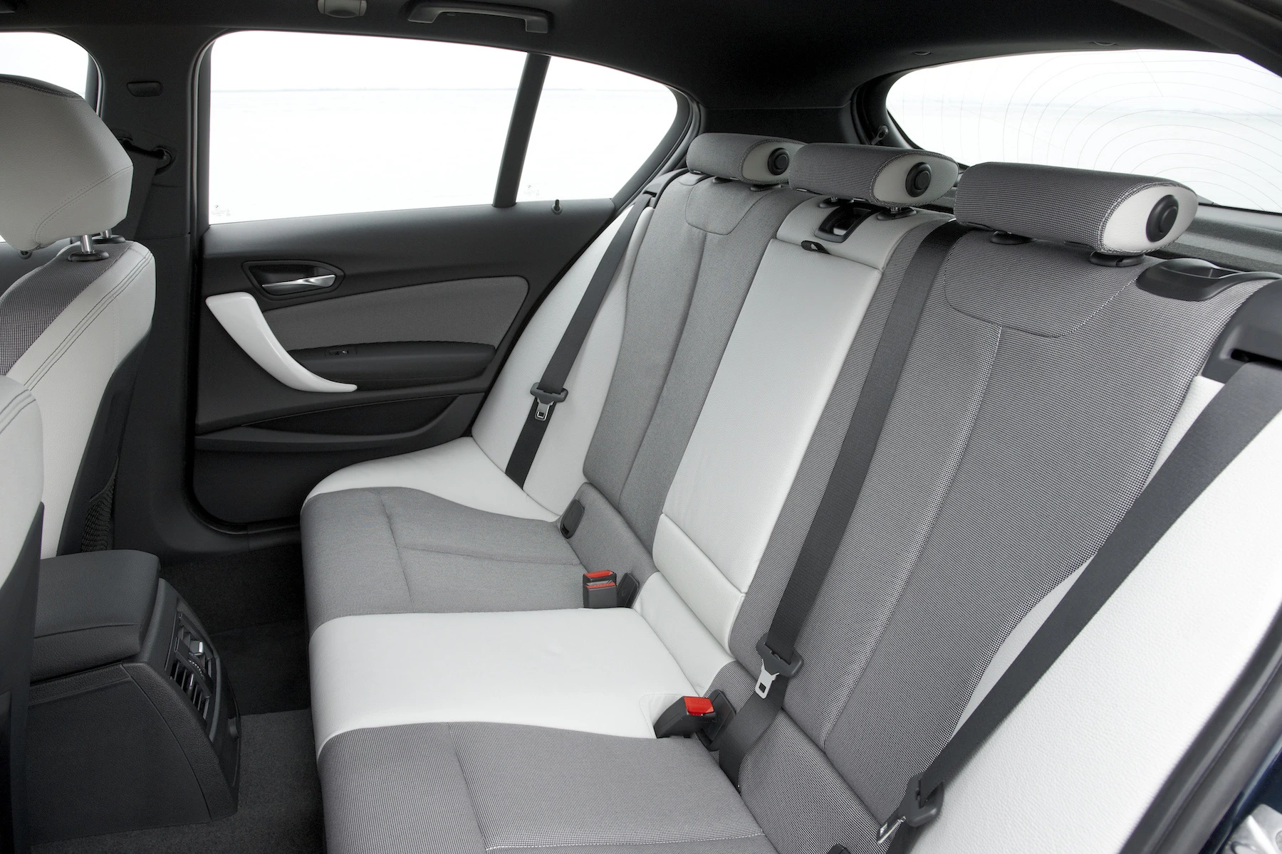 Innenraum eines Autos mit grauen und weißen Sitzen, drei Sicherheitsgurten und einem Mittelarmlehnenfach. Helles, modernes Design.