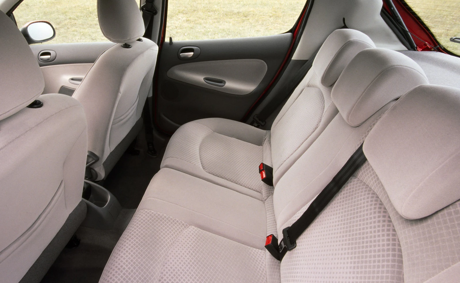 Beige Autoinnenraum mit drei Rücksitzen, Sicherheitsgurten und leicht geöffnetem Fenster. Teppichboden und helle Sitzpolster sind sichtbar.