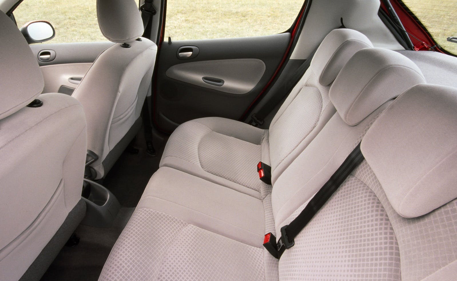 Beige Autoinnenraum mit drei Rücksitzen, Sicherheitsgurten und leicht geöffnetem Fenster. Teppichboden und helle Sitzpolster sind sichtbar.