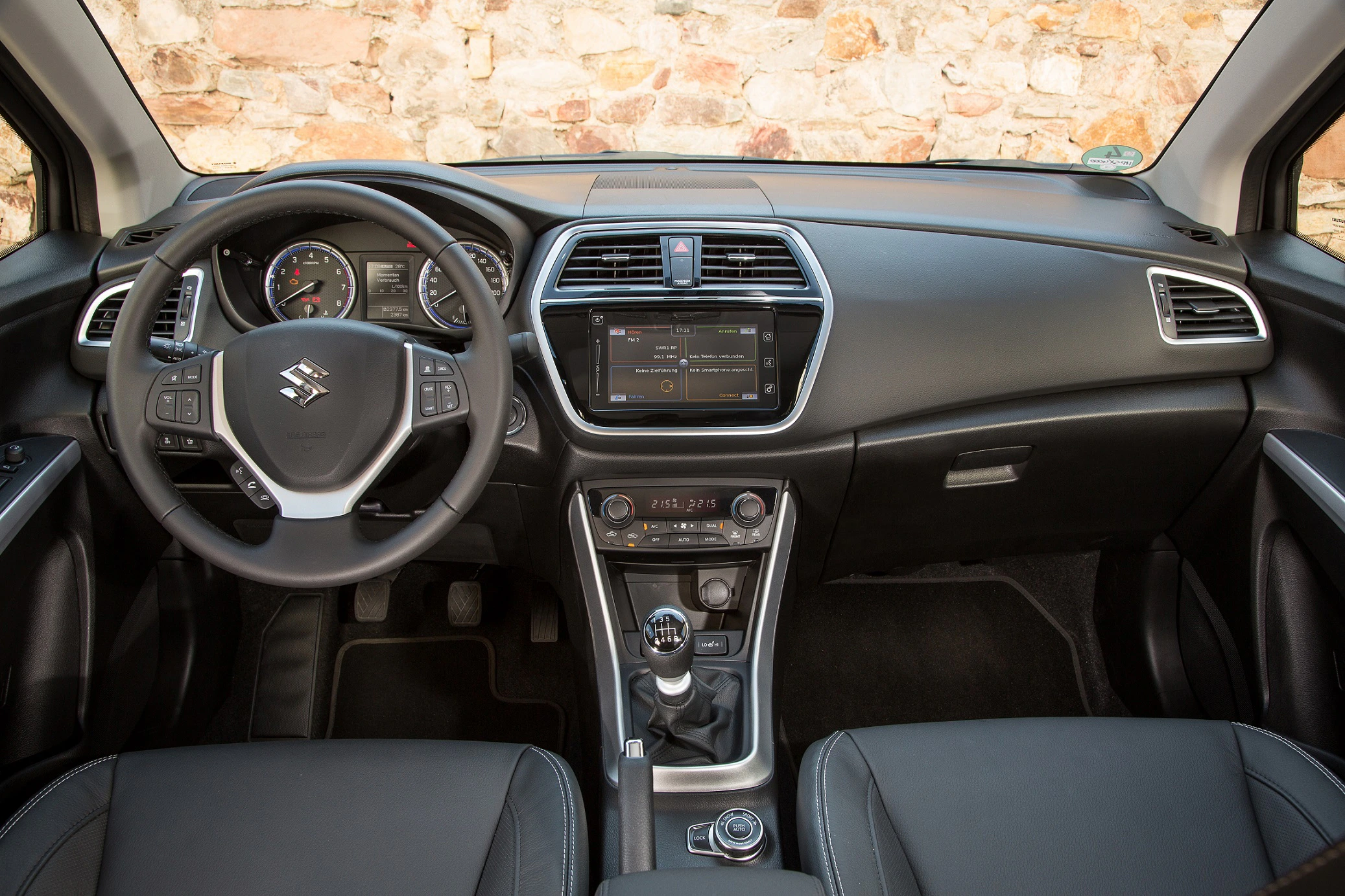 Innenraum eines Autos mit Lenkrad, Armaturenbrett und integriertem Touchscreen. Schaltgetriebe und schwarze Ledersitze sind sichtbar.
