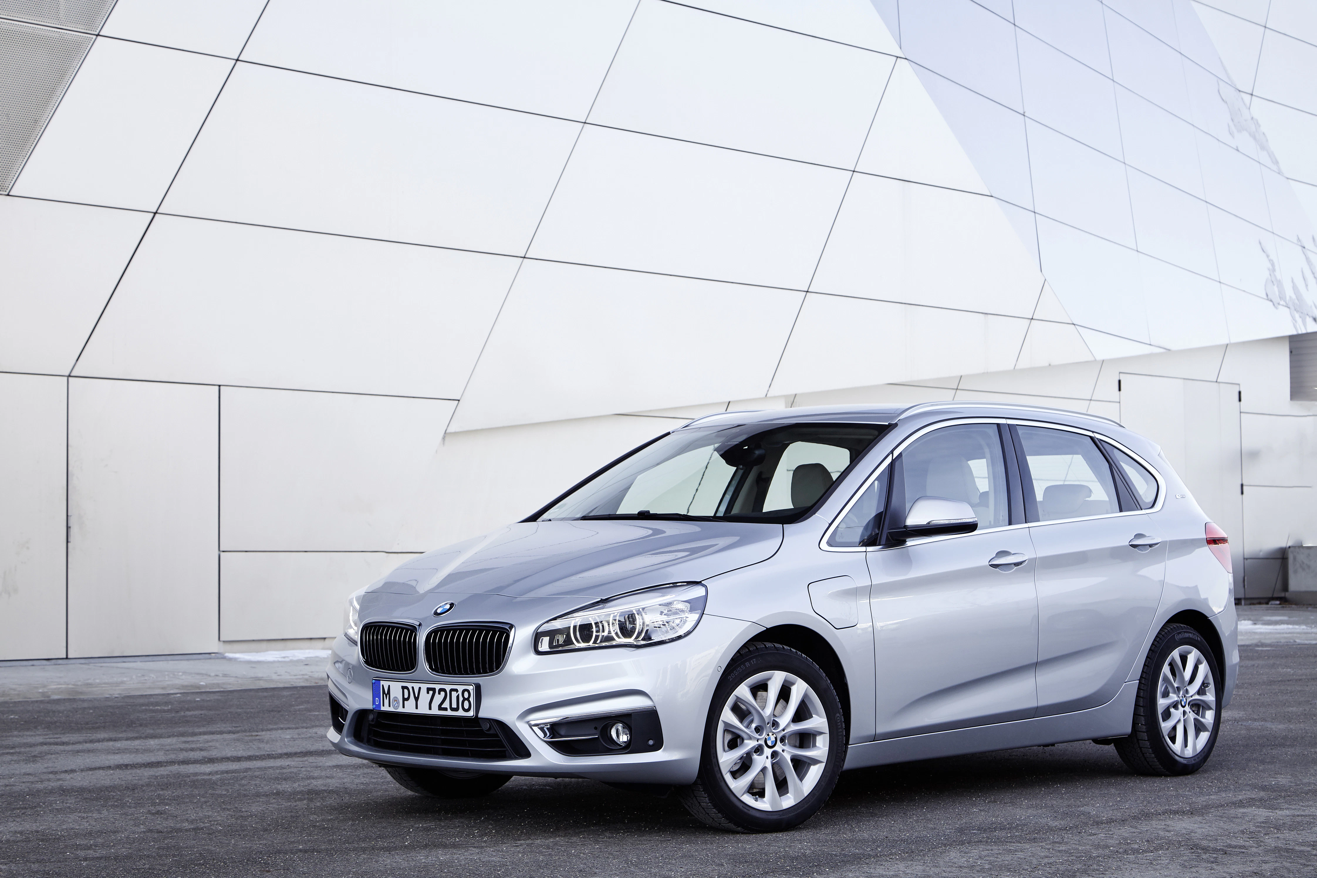 Silberner BMW 2er Active Tourer steht seitlich auf Asphalt vor moderner, weißer Gebäudefassade.