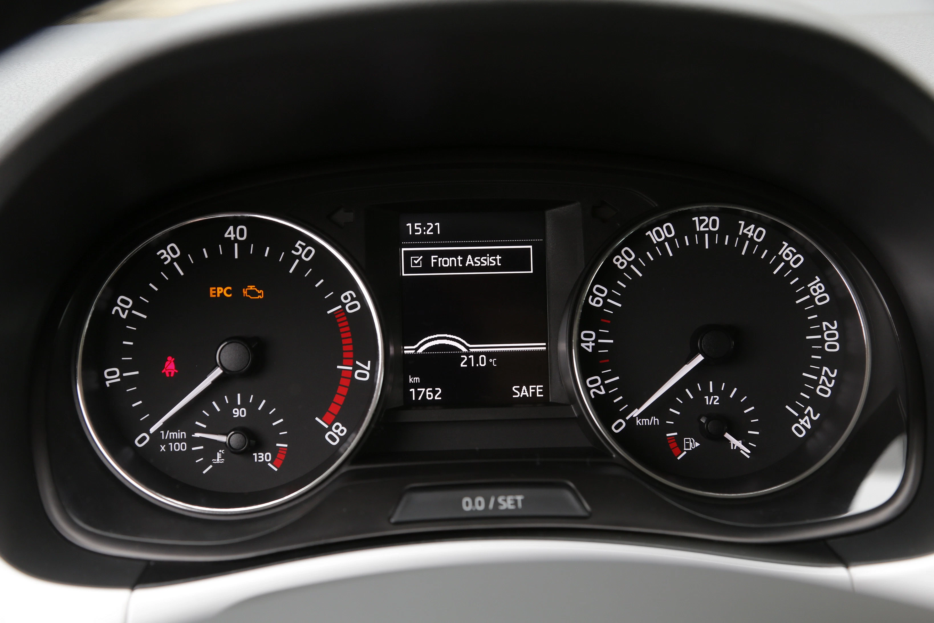 Nahaufnahme eines Autoarmaturenbretts mit Tachometer, Drehzahlmesser und digitalen Anzeigen, die u.a. die Uhrzeit (15:21) und Temperatur (21°C) zeigen.
