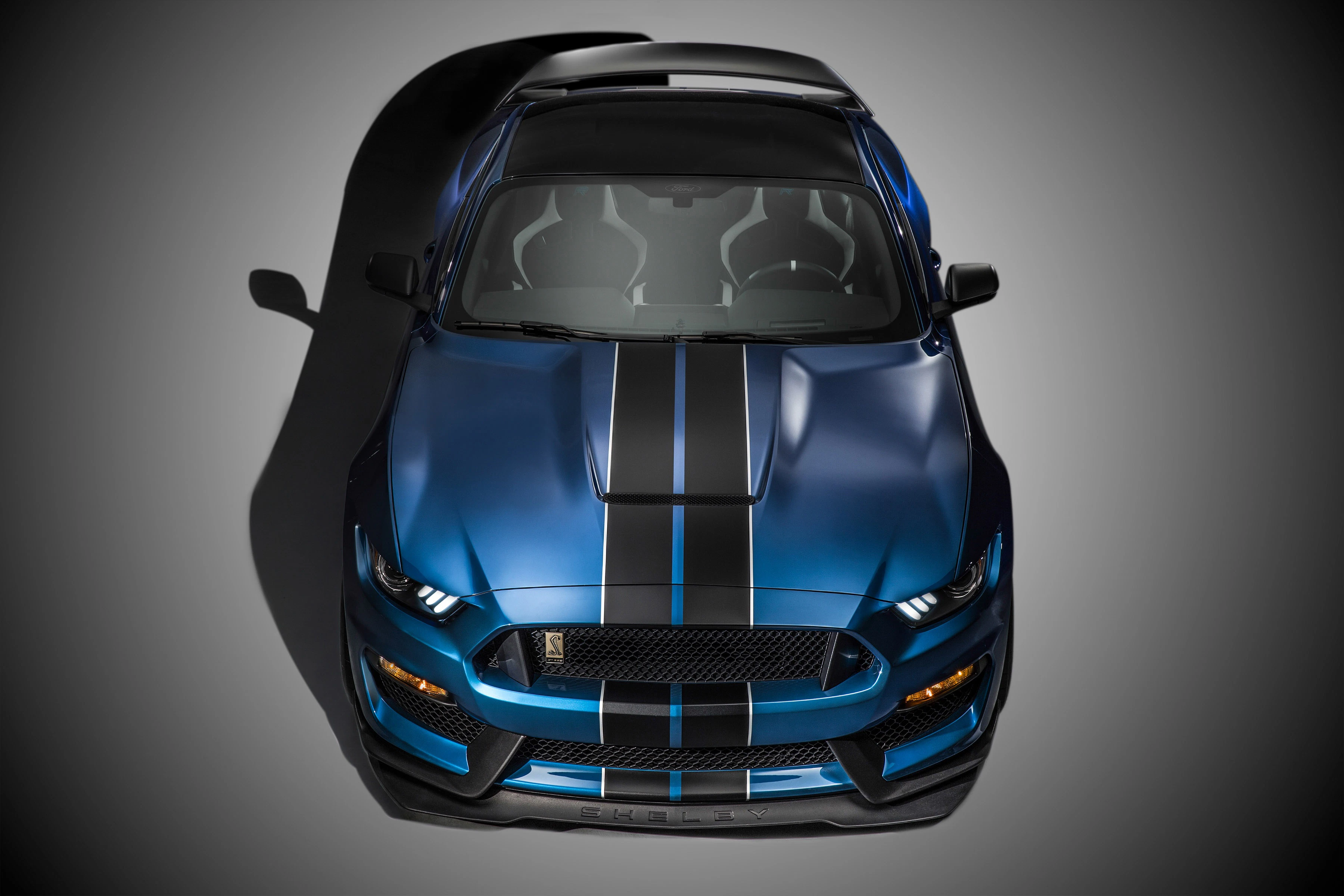 Blauer Sportwagen von oben, mit schwarzen Streifen über die Motorhaube und sportlichem Design. Schatten auf grauem Hintergrund.