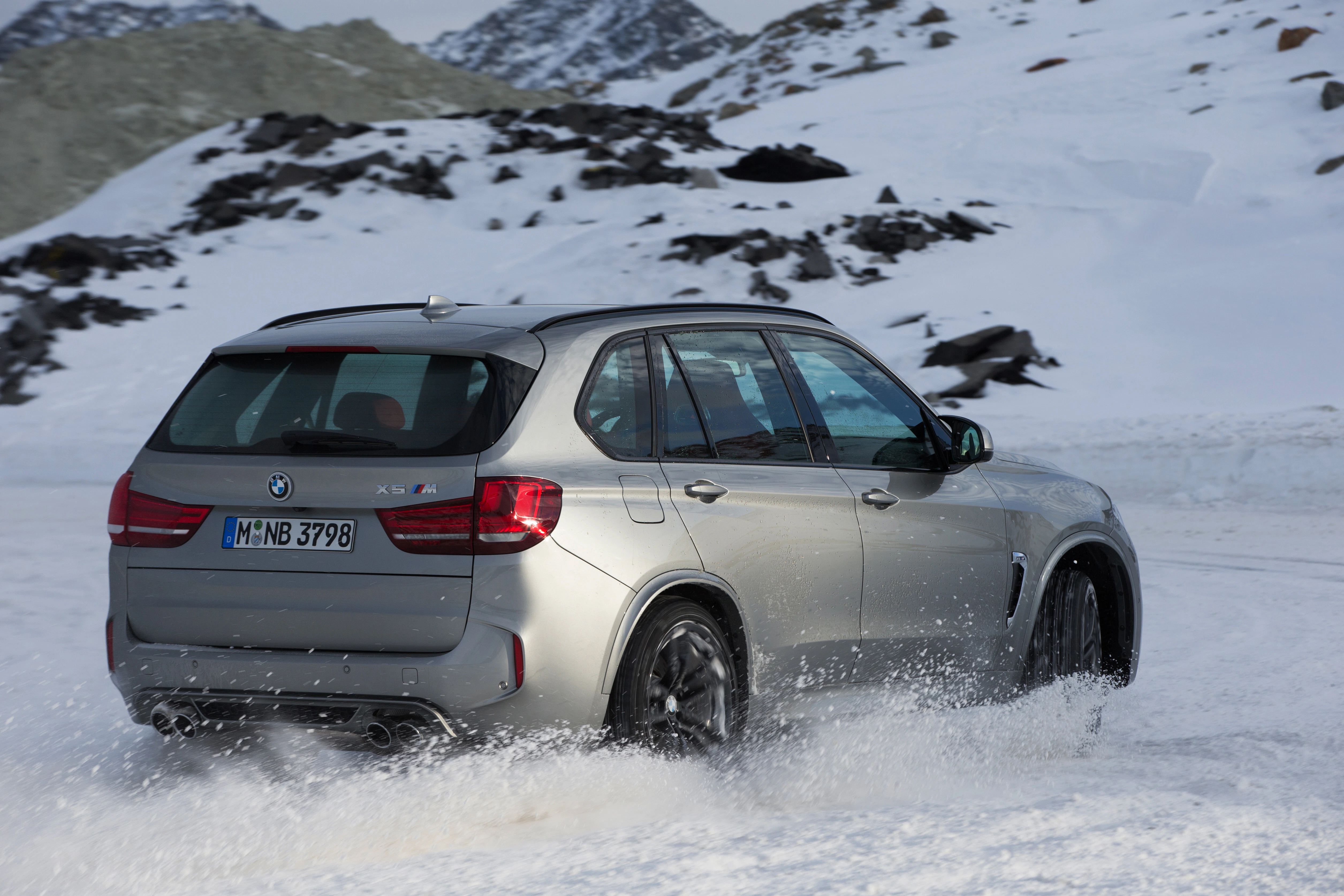 Silberner SUV fährt auf schneebedeckter Straße in winterlicher Berglandschaft. Dynamische Bewegung, Schnee spritzt hinter dem Auto auf.