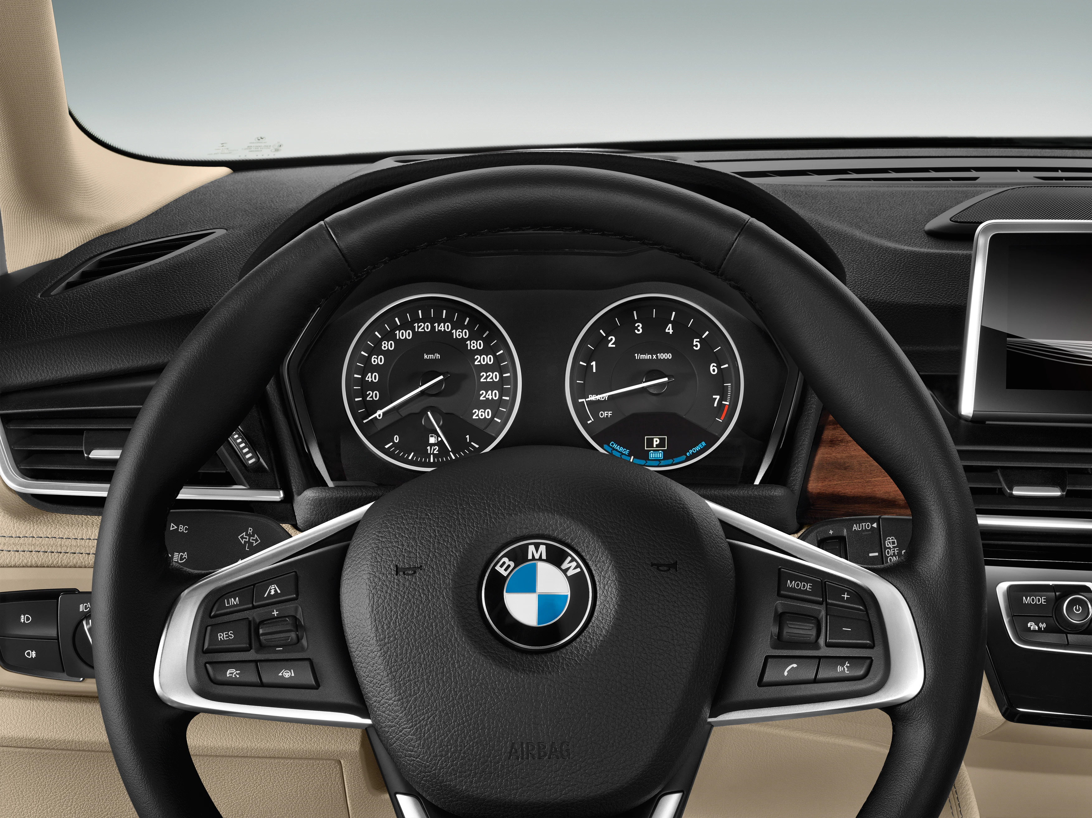 Lenkrad eines BMW mit Tacho und Drehzahlmesser im Hintergrund. Multifunktionstasten am Lenkrad, Display rechts im Armaturenbrett.