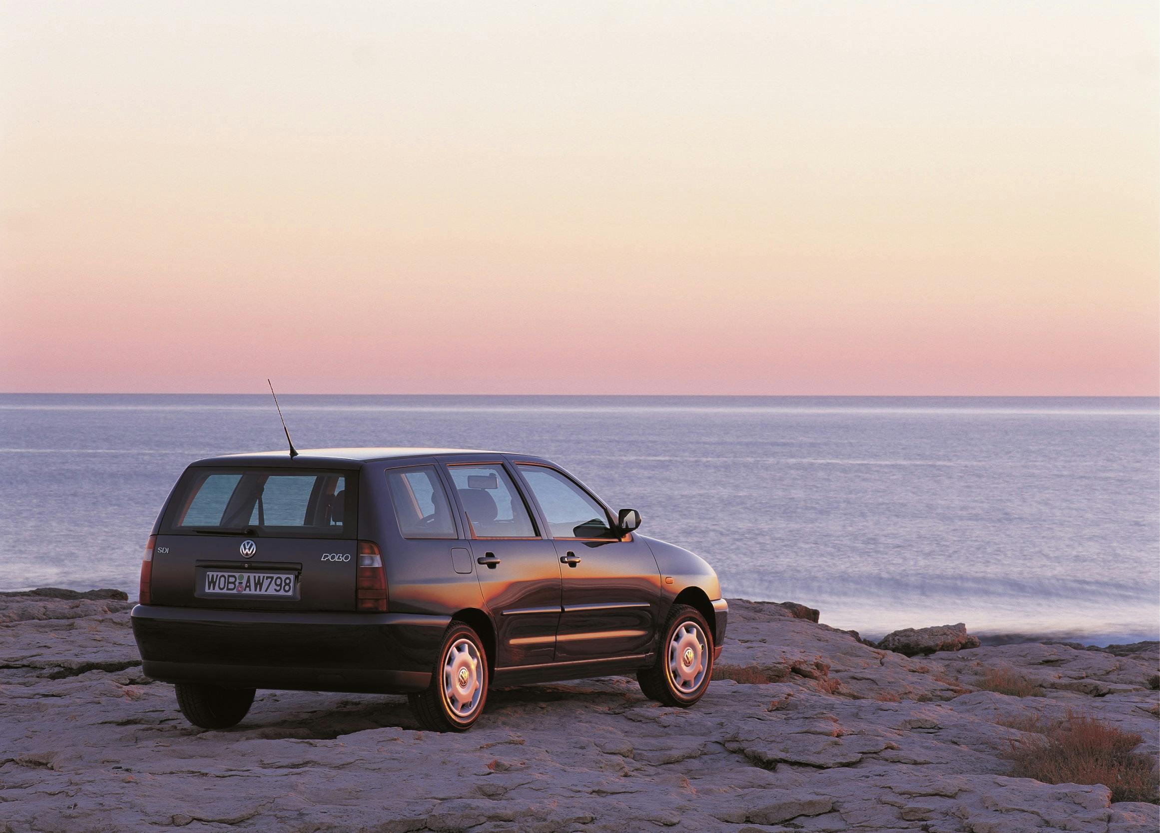 Ein schwarzer VW Polo steht bei Sonnenuntergang auf einem Felsen am Meer, der Himmel schimmert in sanften Pastellfarben.