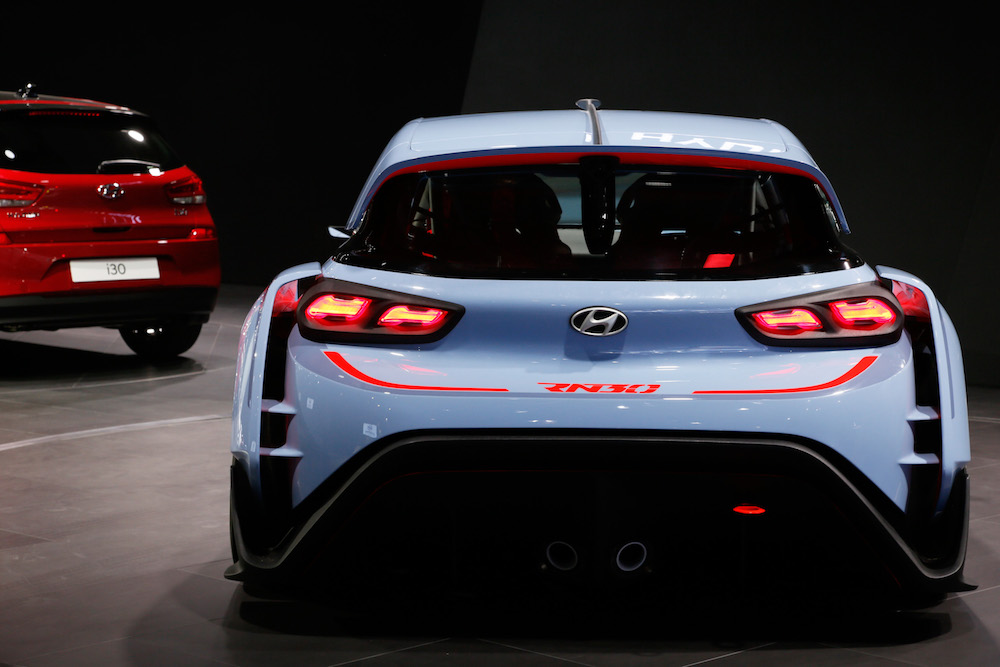 Rückansicht eines sportlichen blauen Hyundai RN30 mit markanten Rückleuchten auf einem Autosalon, links rotes Hyundai-Modell zu sehen.