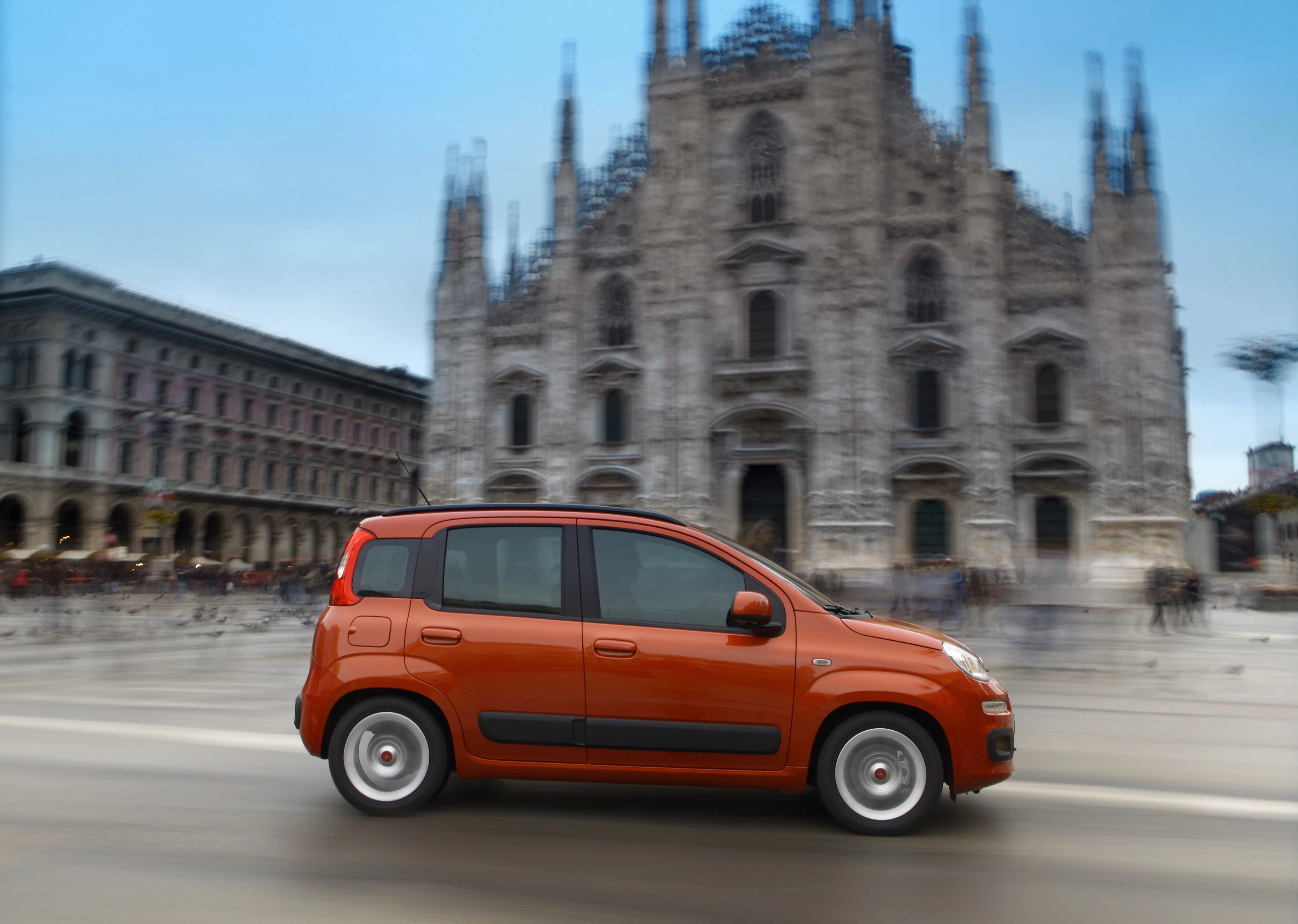 Oranges Auto fährt an einer neogotischen Kathedrale vorbei, unscharfer Hintergrund.