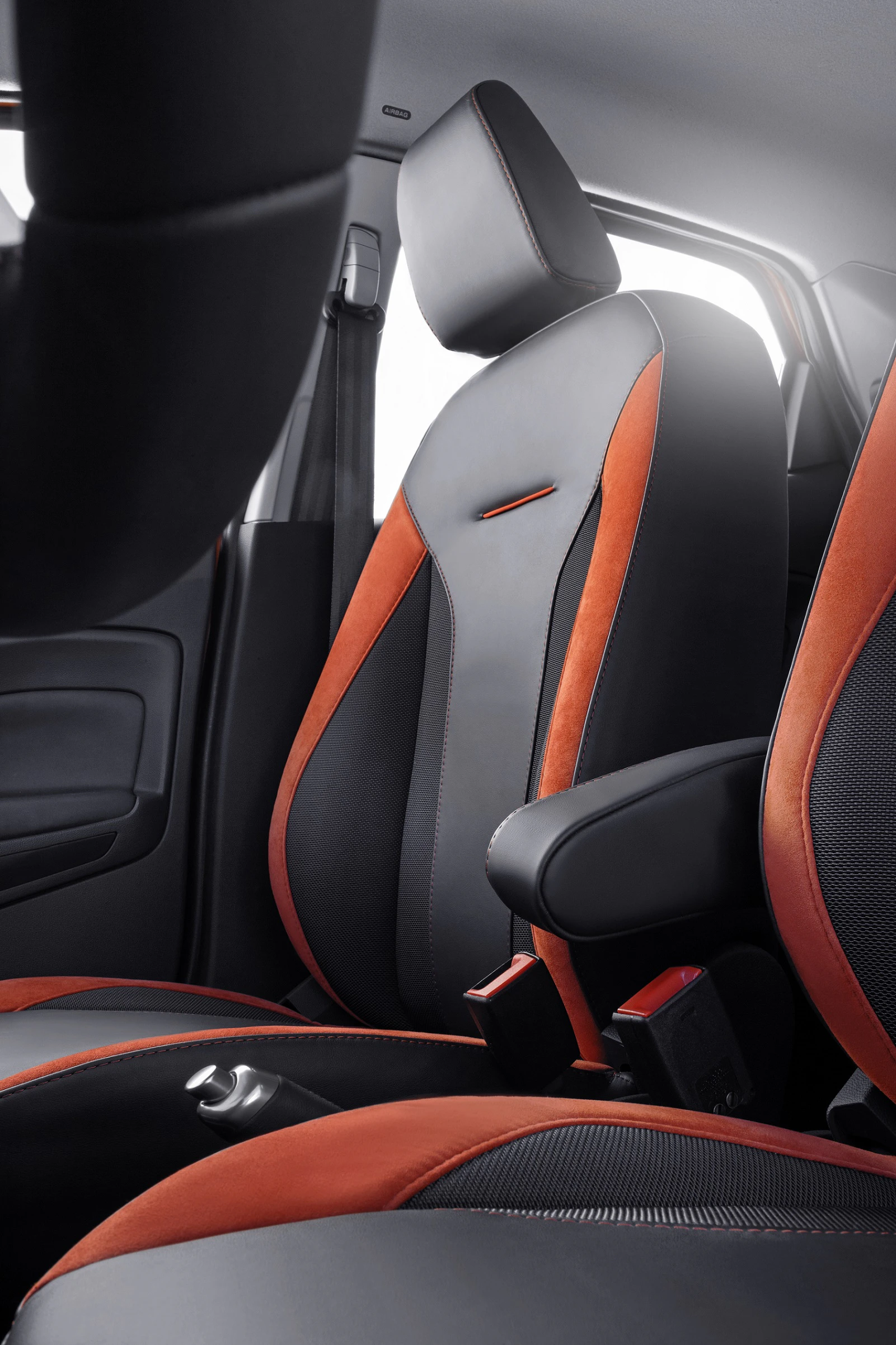 Vordersitze eines Autos mit schwarz-orangefarbenem Stoff, Armlehne und Türdetail. Moderner Innenraum mit klaren Linien und Texturen.