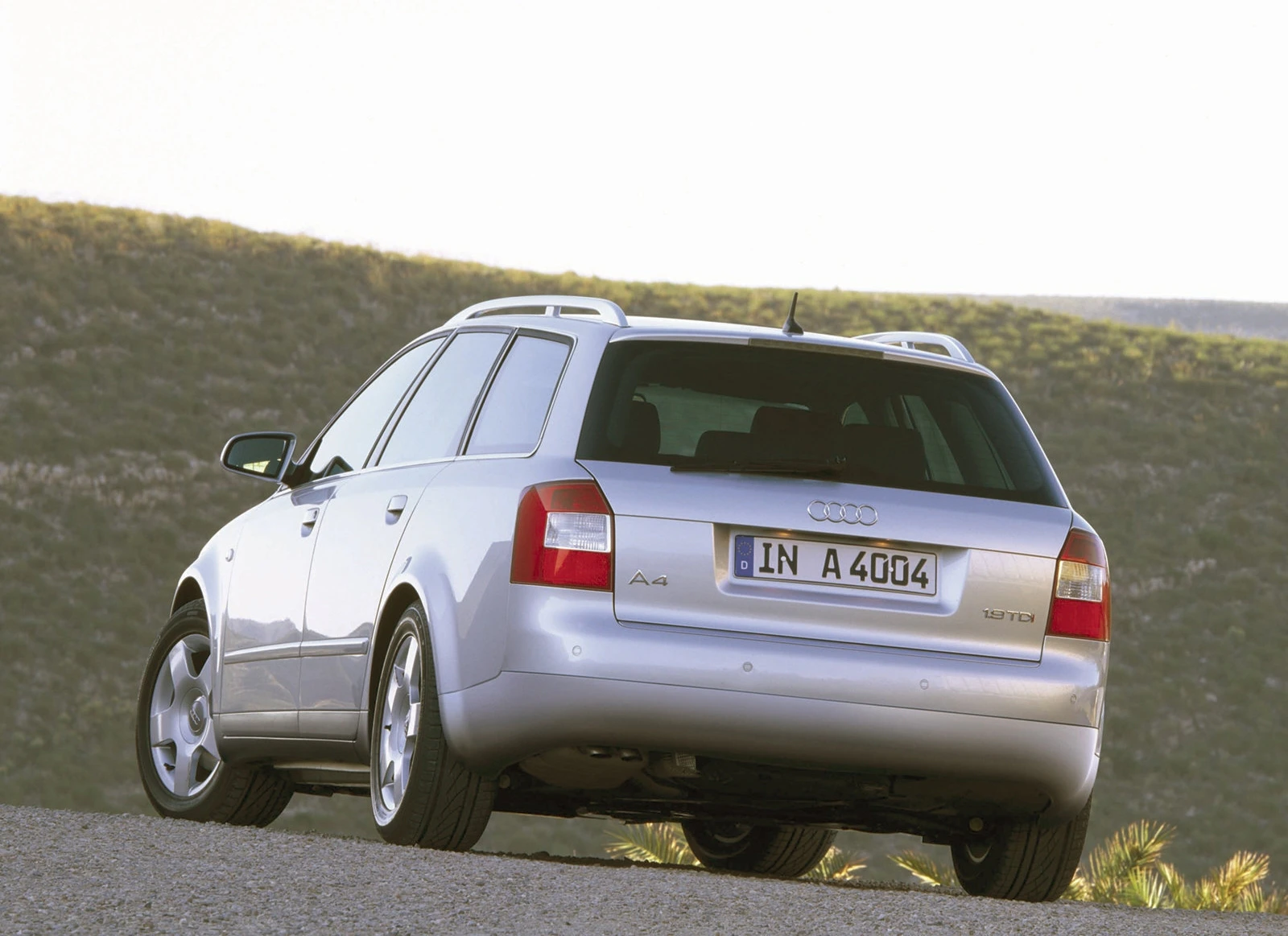Silberner Kombi-Auto, vermutlich Audi A4, parkt auf Schotterweg, Hintergrund: Hügel und blauer Himmel.
