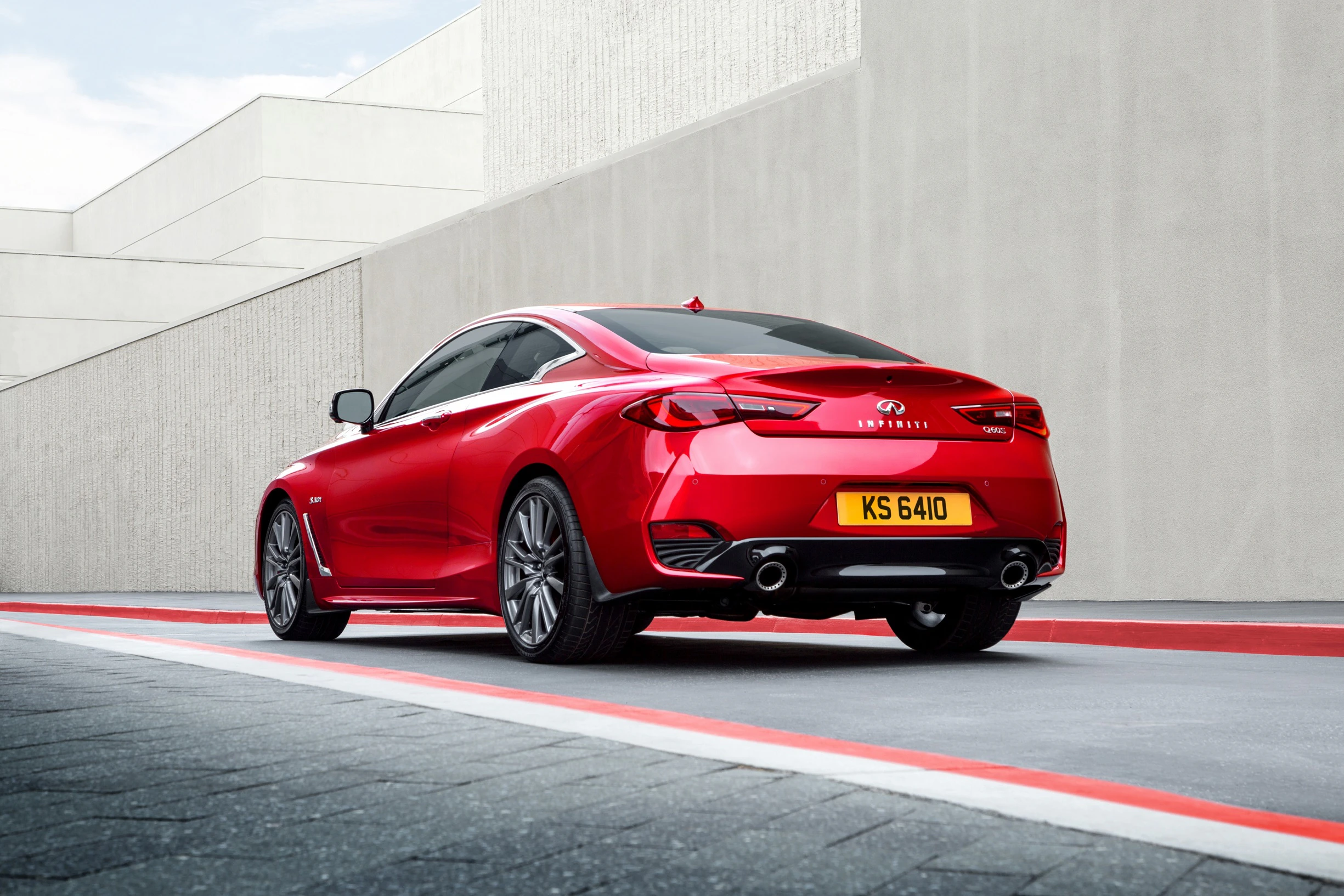 Rotes Sportcoupé auf grauem Pflaster vor moderner, heller Gebäude-Kulisse, mit deutschem Kennzeichen "KS 6410".