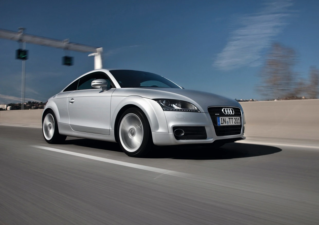Silberner Audi TT fährt auf einer Autobahn bei klarem Himmel. Dynamische Bewegung betont durch die verschwommene Fahrbahn.