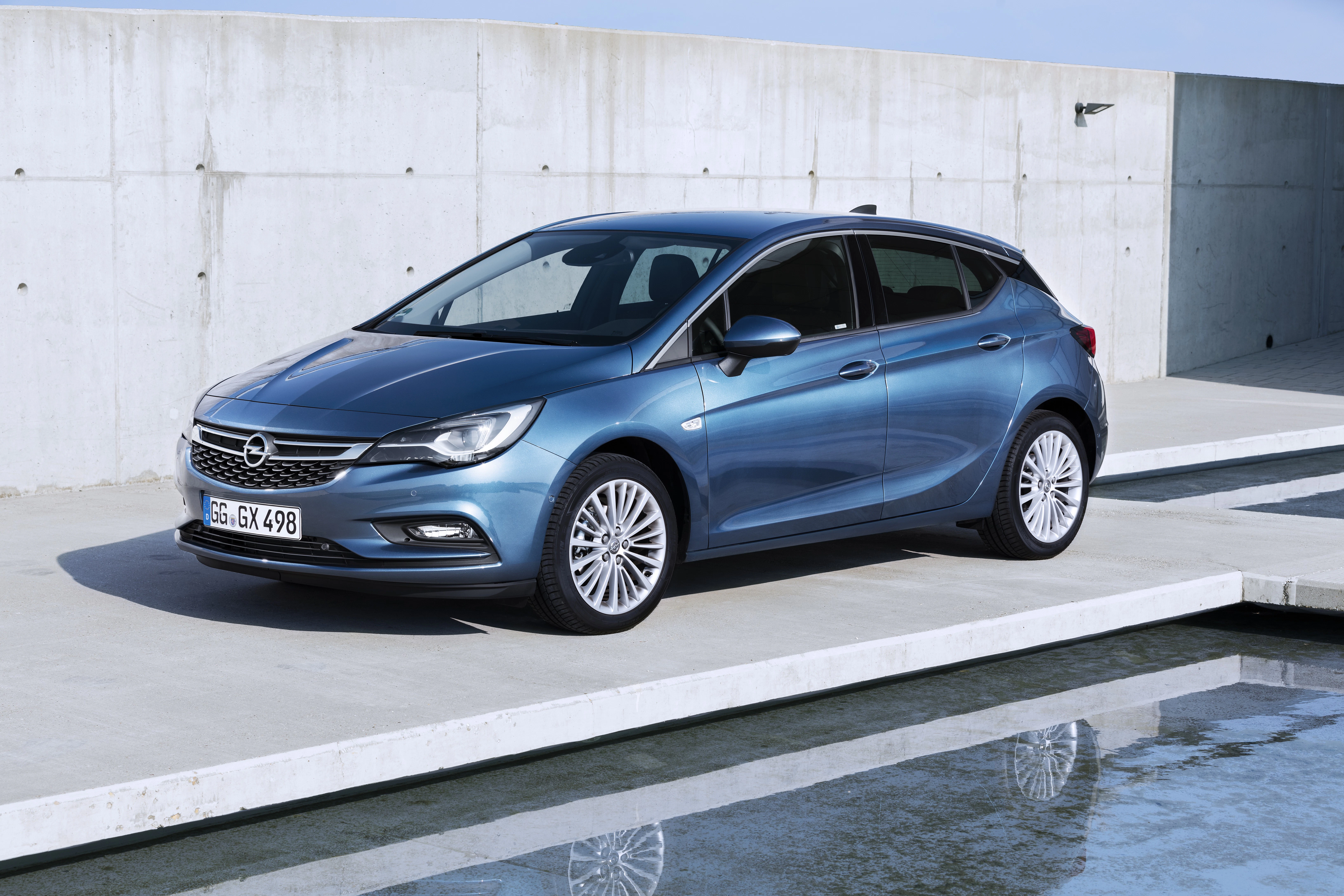 Blauer Opel Astra parkt auf modernem, minimalistischen Betonuntergrund neben einem Wasserbecken bei klarem Himmel.