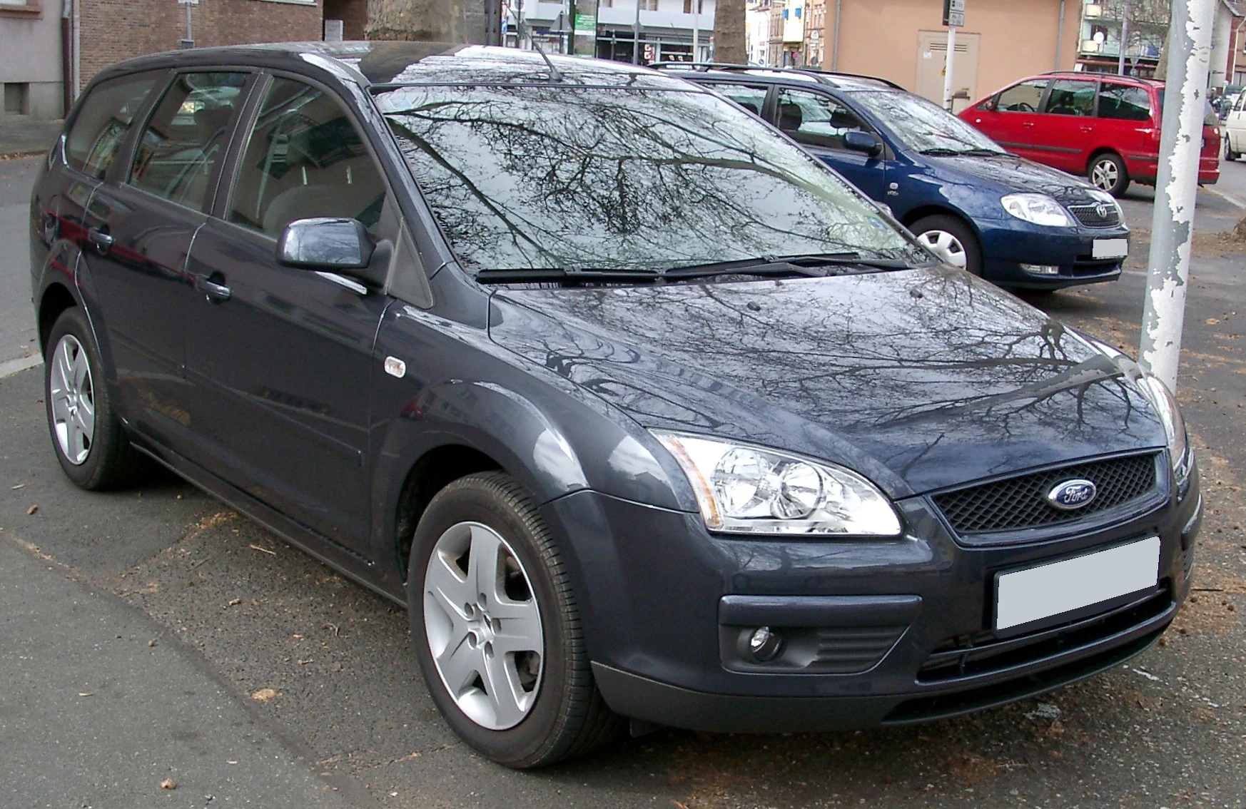 Grauer Kombi-Pkw, Ford Focus, auf Parkplatz; Hintergrund: rote und blaue Autos.
