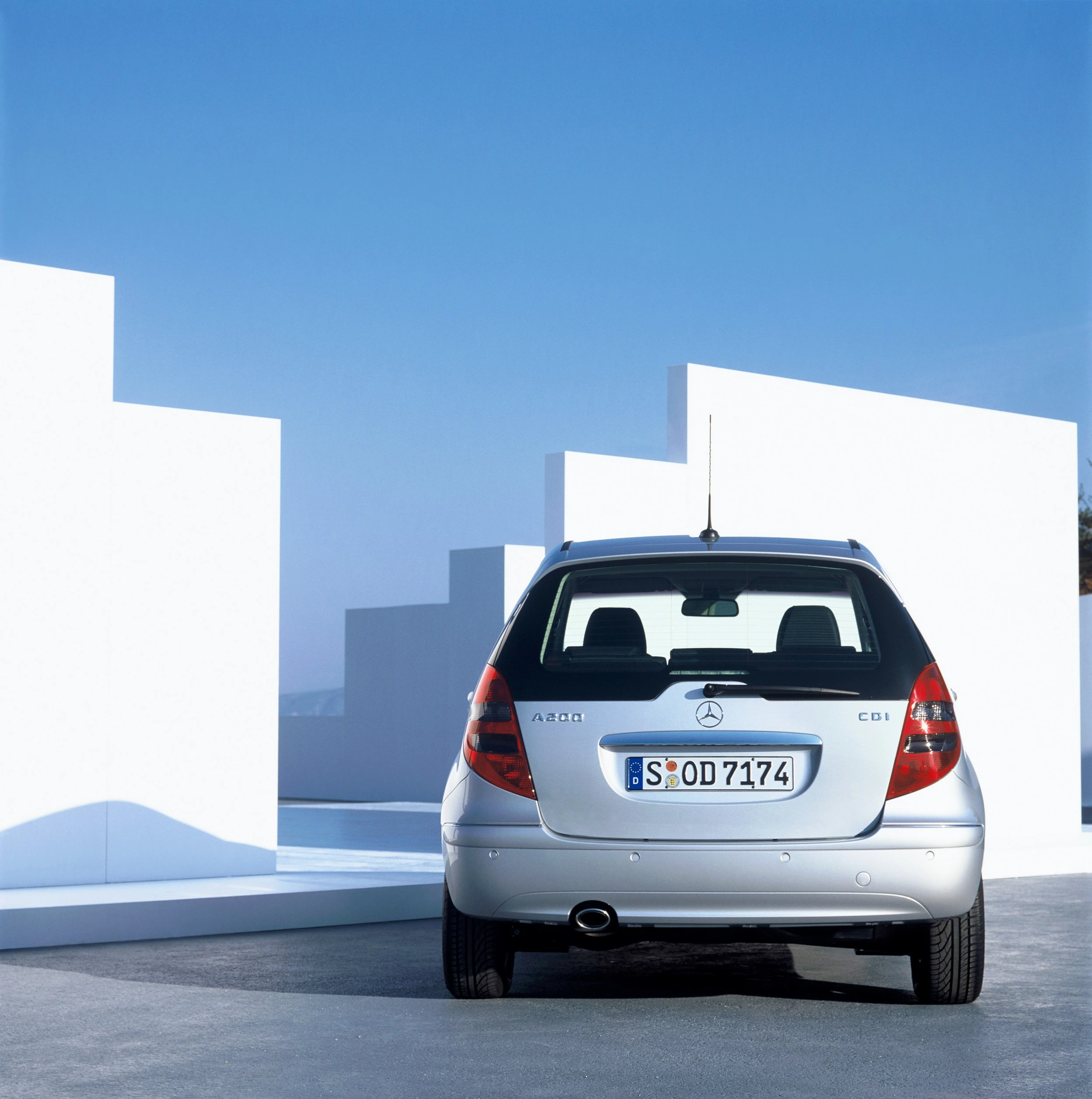 Silberner Mercedes A 200 CDI vor modernen weißen Gebäuden bei blauem Himmel. Rückansicht des Autos auf grauem Boden.