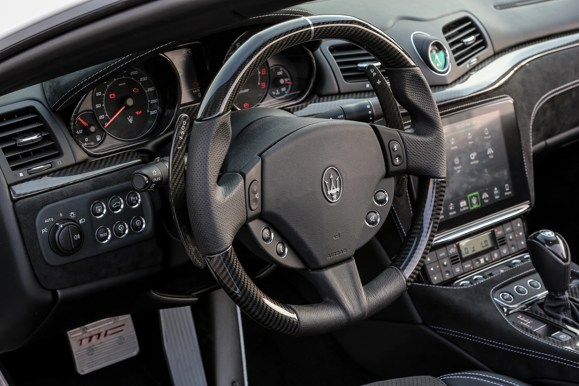 Innenraum eines Maserati mit luxuriösem Armaturenbrett, Lederlenkrad, Tachometern und großem Infotainment-Display.