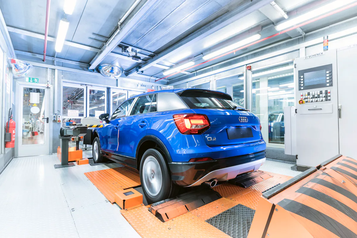 Blaues Auto in moderner Werkstatt auf Prüfstand. Technik und Monitore umgeben das Fahrzeug zur Inspektion oder Wartung.