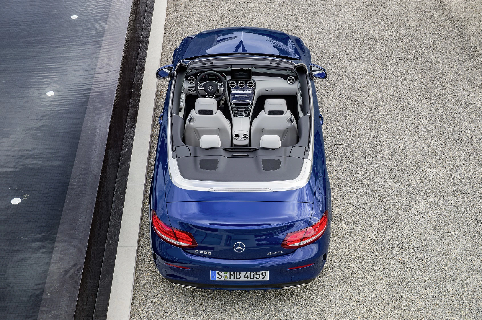 Blaues Mercedes-Cabriolet von oben, geparkt neben Wasseroberfläche, offen, mit hellem Innenraum und zwei Sitzen.