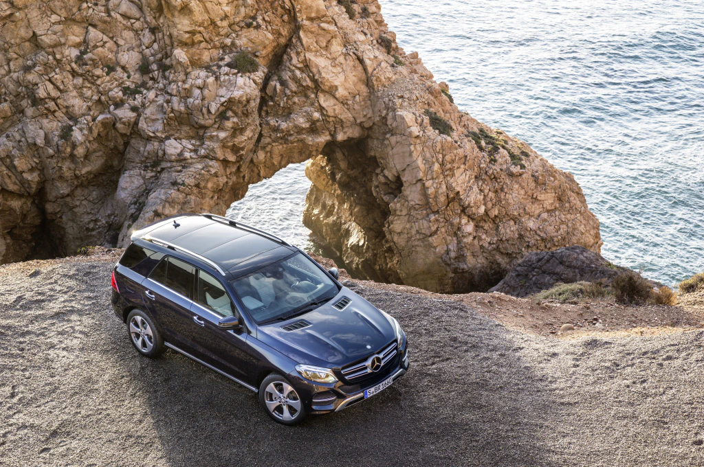 SUV geparkt auf einer felsigen Klippe mit Blick aufs Meer, im Hintergrund natürliche Felsformation und Wellen, sonniges Wetter.