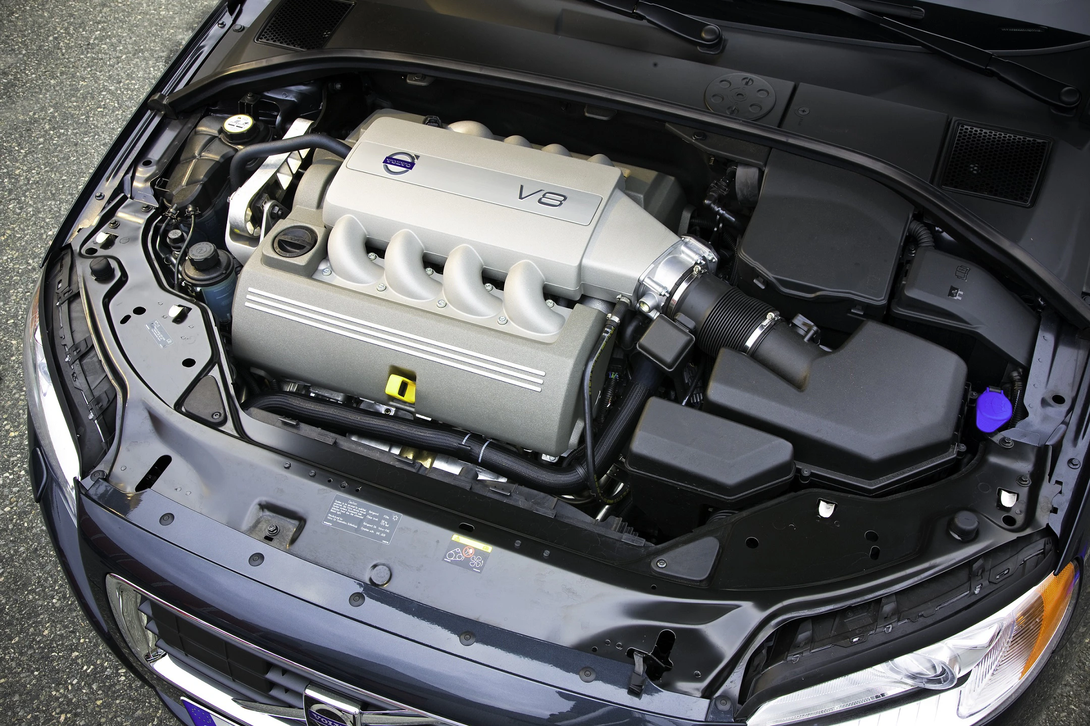 Volvo Motorraum mit V8-Motor, sauber und ordentlich angeordnet, mit silbernen und schwarzen Komponenten auf einem grauen Hintergrund.