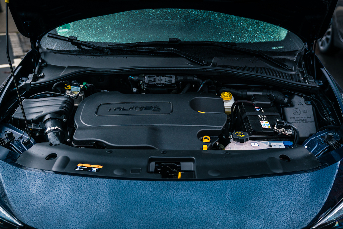 Motorraum eines Autos mit offenem Deckel, der einen modernen Motor und verschiedene Autoteile zeigt.