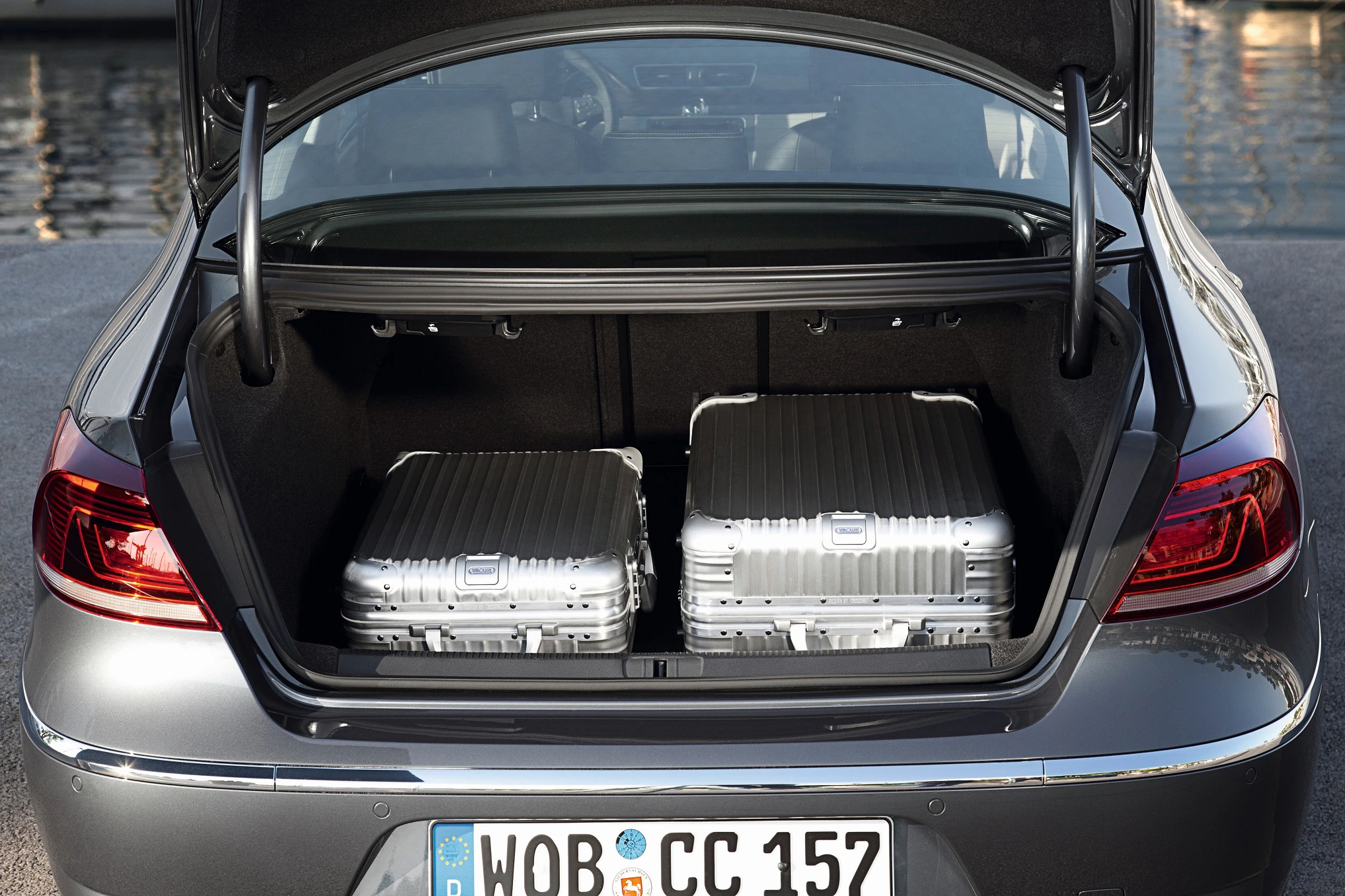 Offener Kofferraum eines Autos mit zwei silbernen Koffern. Nummernschild und Rücklichter sind sichtbar.