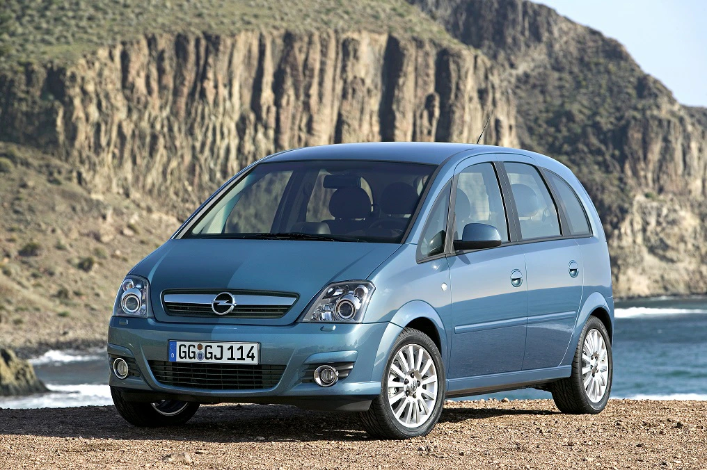 Ein blauer Opel Meriva parkt auf einer Klippe mit felsiger Landschaft und Meer im Hintergrund.