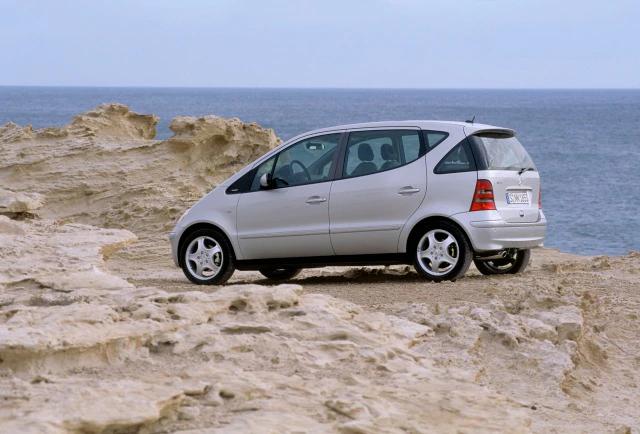 Silberner Minivan parkt an einer felsigen Küste mit Blick auf das Meer unter klarem Himmel.