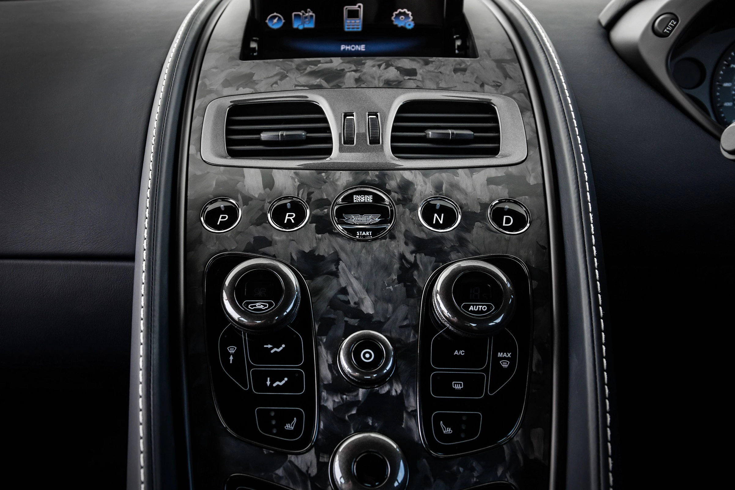 Nahaufnahme einer luxuriösen Autokonsole mit schwarzem Marmorfinish, mehreren Knöpfen, Lüftungsschlitzen und einem kleinen Display oben.