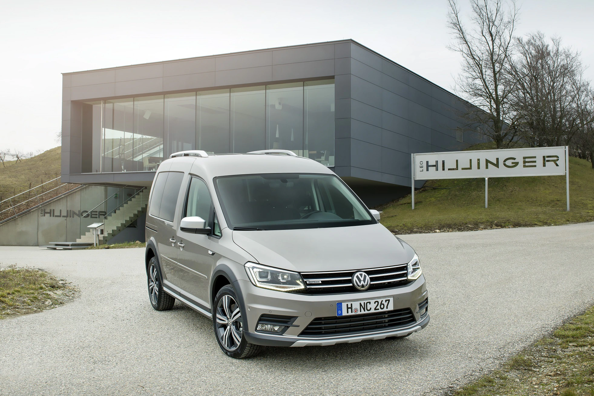 Ein silberner VW Caddy parkt vor einem modernen Gebäude mit Glasfassade und der Beschriftung "Hillingser".