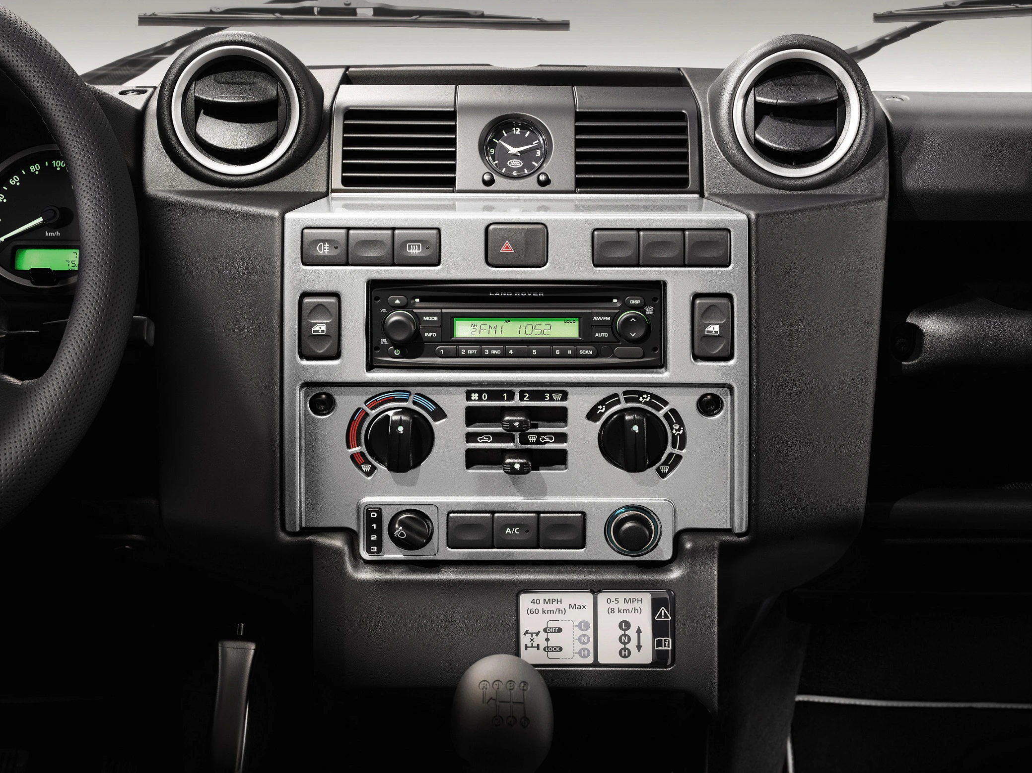 Armaturenbrett eines Fahrzeugs mit Klimaanlage, Radio und Bedienknöpfen. Das Design ist funktional und symmetrisch aufgebaut.