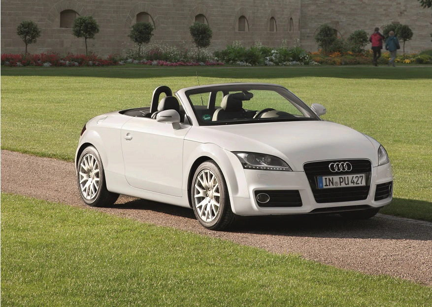 Weißes Audi Cabriolet steht auf einem Kiesweg, umgeben von grüner Rasenfläche und alten Mauern im Hintergrund.