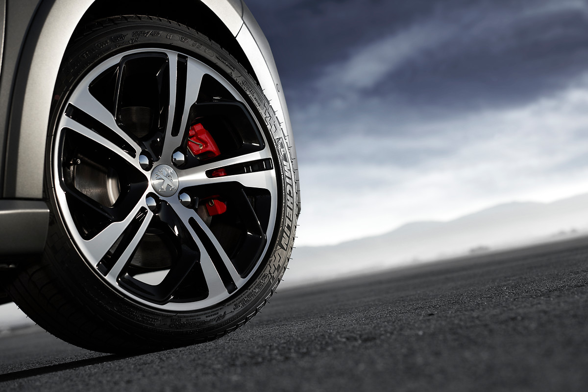 Nahaufnahme eines Autoreifens mit sportlicher Felge und roten Bremssätteln vor bewölktem Himmel.