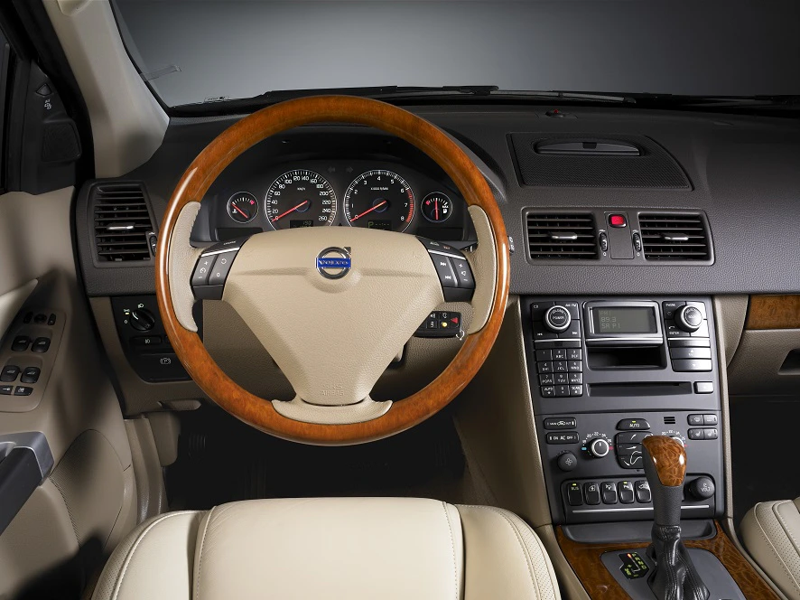 Innenraum eines Autos mit beigem Leder, Holzlenkrad und moderner Instrumententafel und Mittelkonsole mit zahlreichen Bedienelementen.