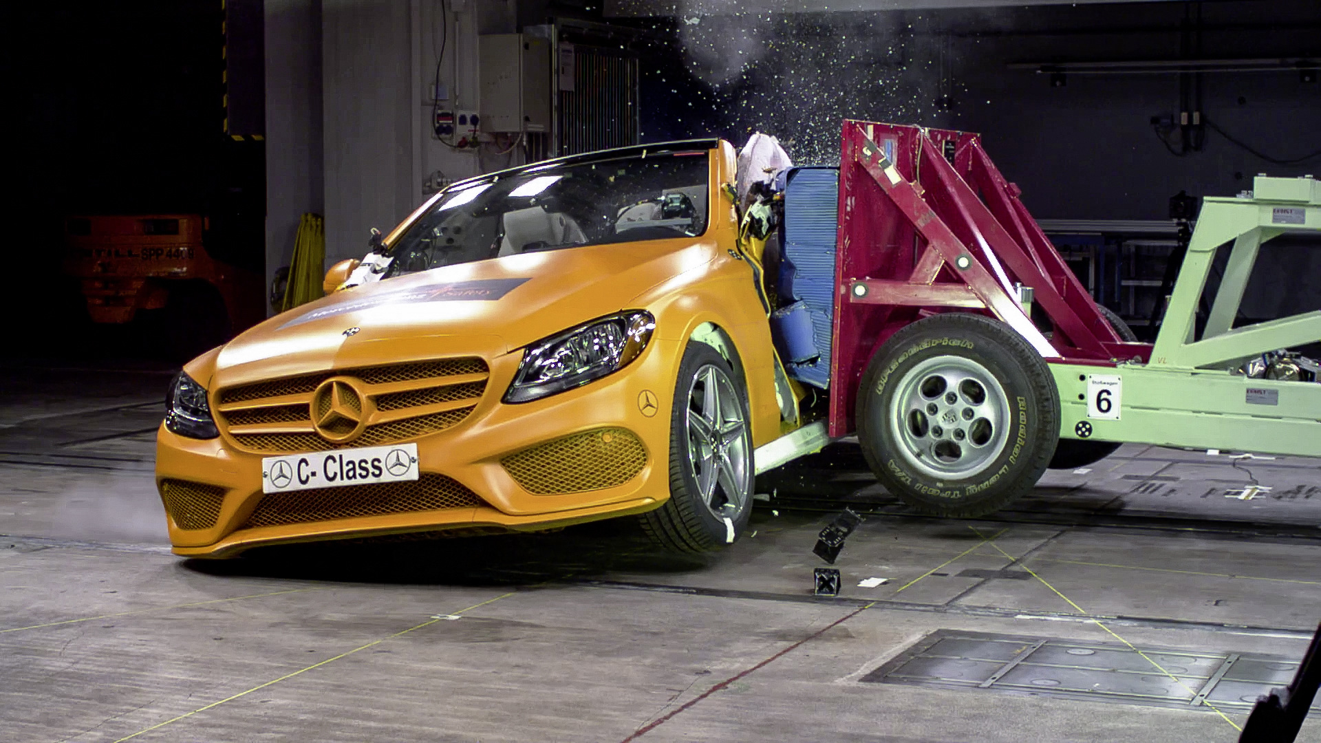 Ein orangefarbenes Auto durchläuft einen Crashtest. Es kollidiert mit einem Hindernis, während ein Dummy im Fahrzeugsitz sitzt.