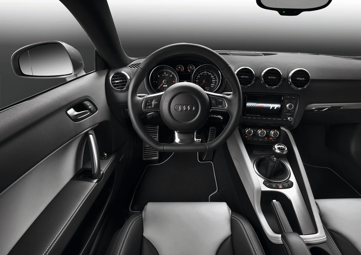 Innenraum eines modernen Audi mit schwarzem Leder, Multifunktionslenkrad, sportlichen Rundinstrumenten und zentralem Bildschirm auf grauem Hintergrund.