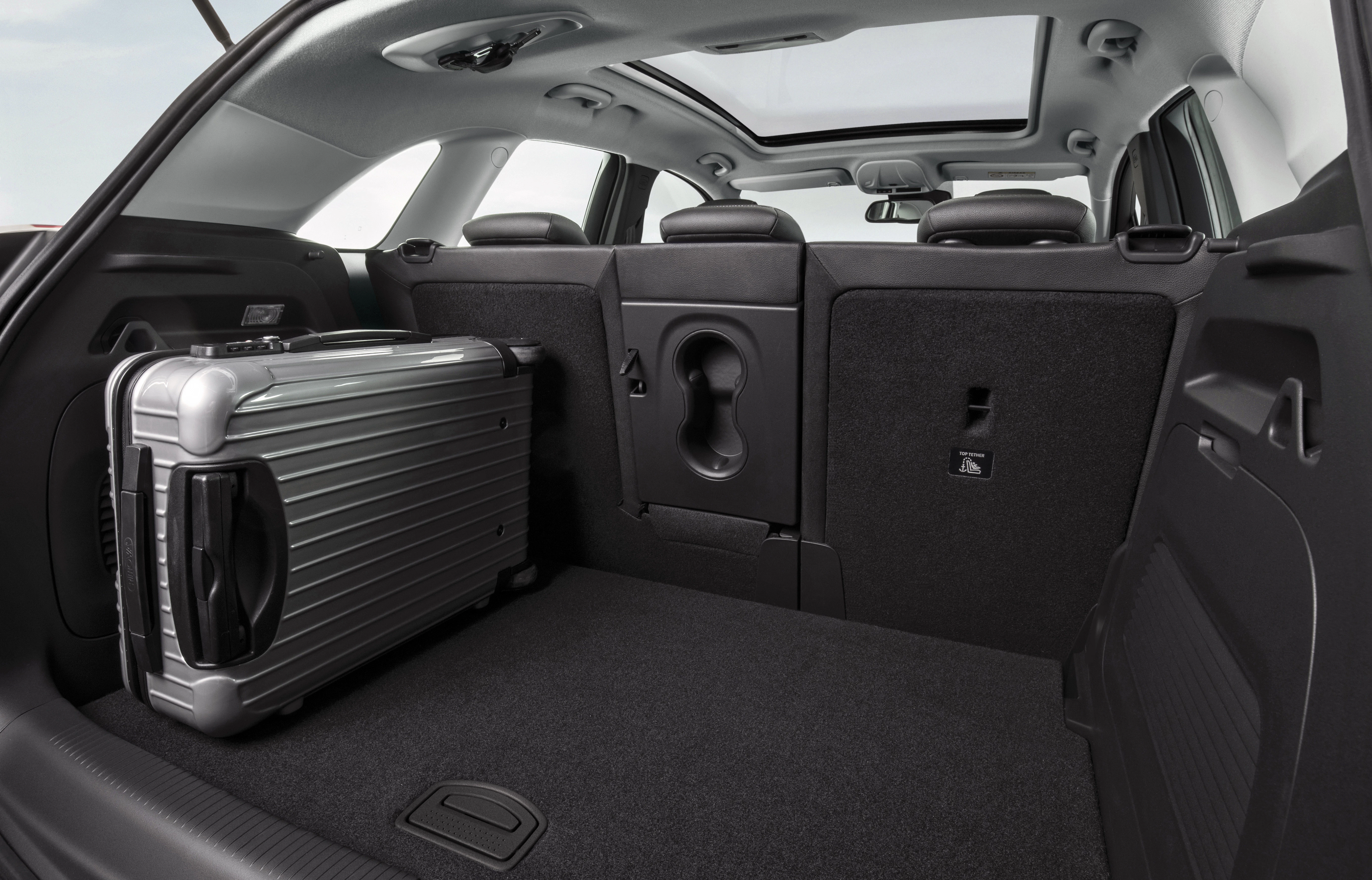 Kofferraum eines Autos mit einer großen silbernen Reisetasche, umgeklapptem Sitz und Blick durch das Panoramadach.
