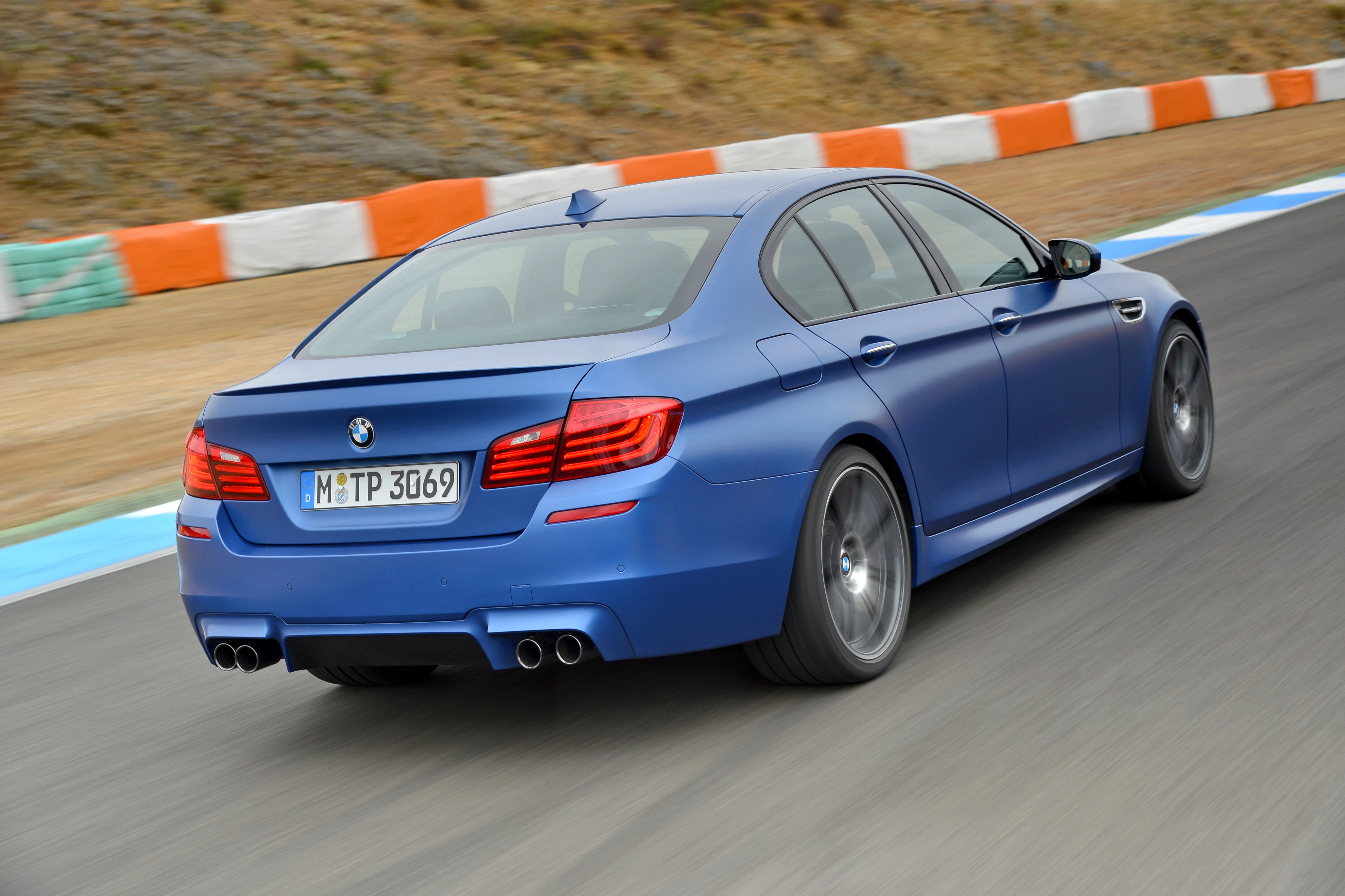 Blauer BMW M5 fährt auf Rennstrecke, links Kurvenbegrenzung. Sportlimousine in dynamischer Fahrtperspektive.